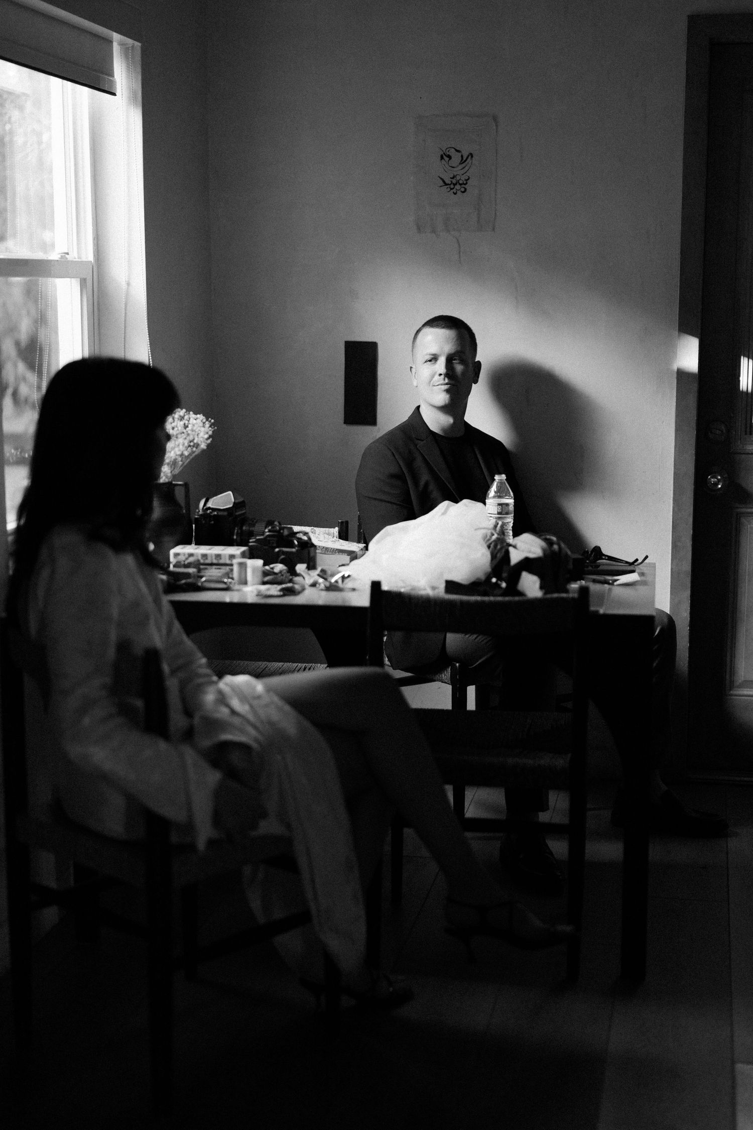 Moody black and white interior scene with figures seated in dim lighting.