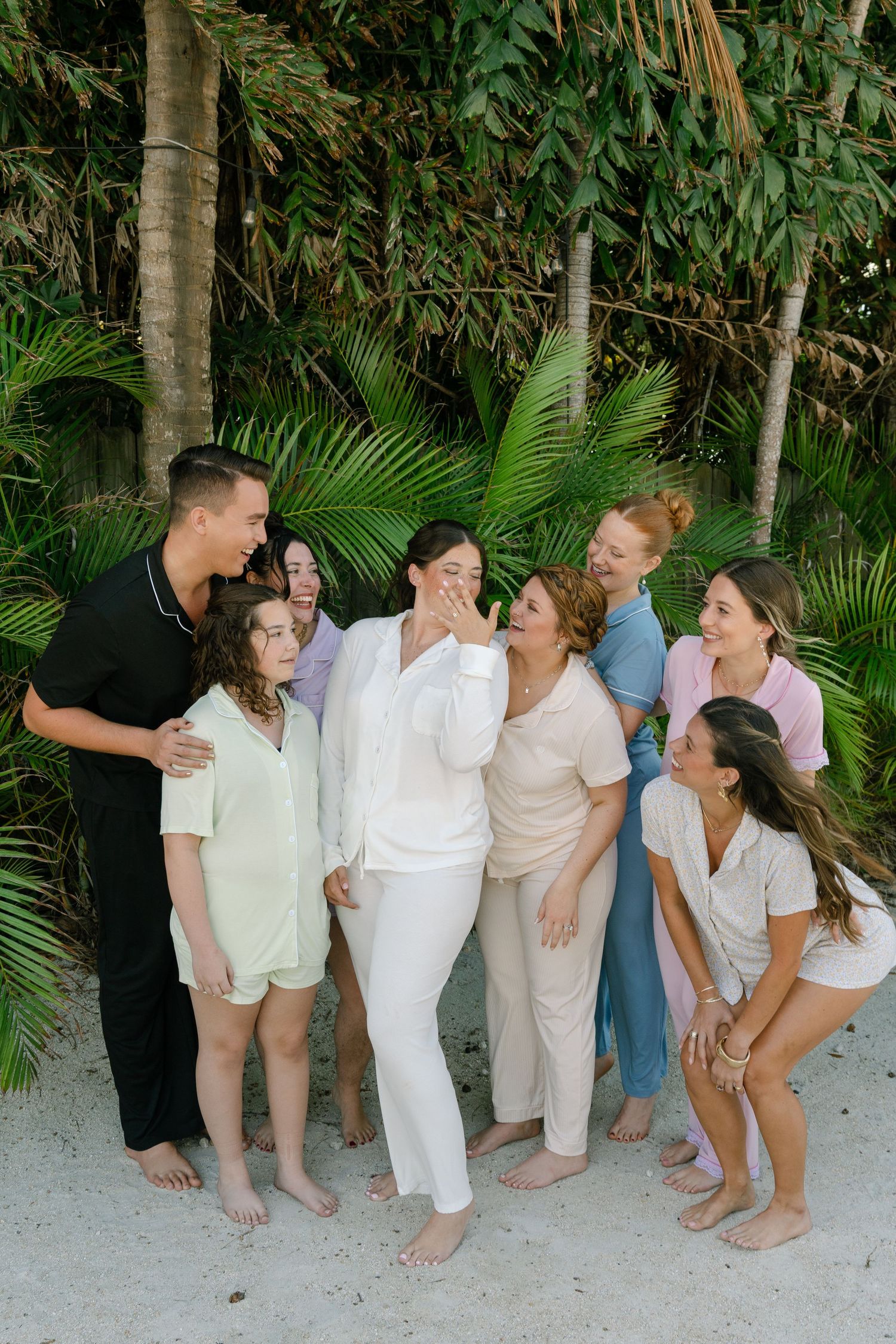 A group of people, including adults and children, standing together in a tropical setting with palm trees in the background.