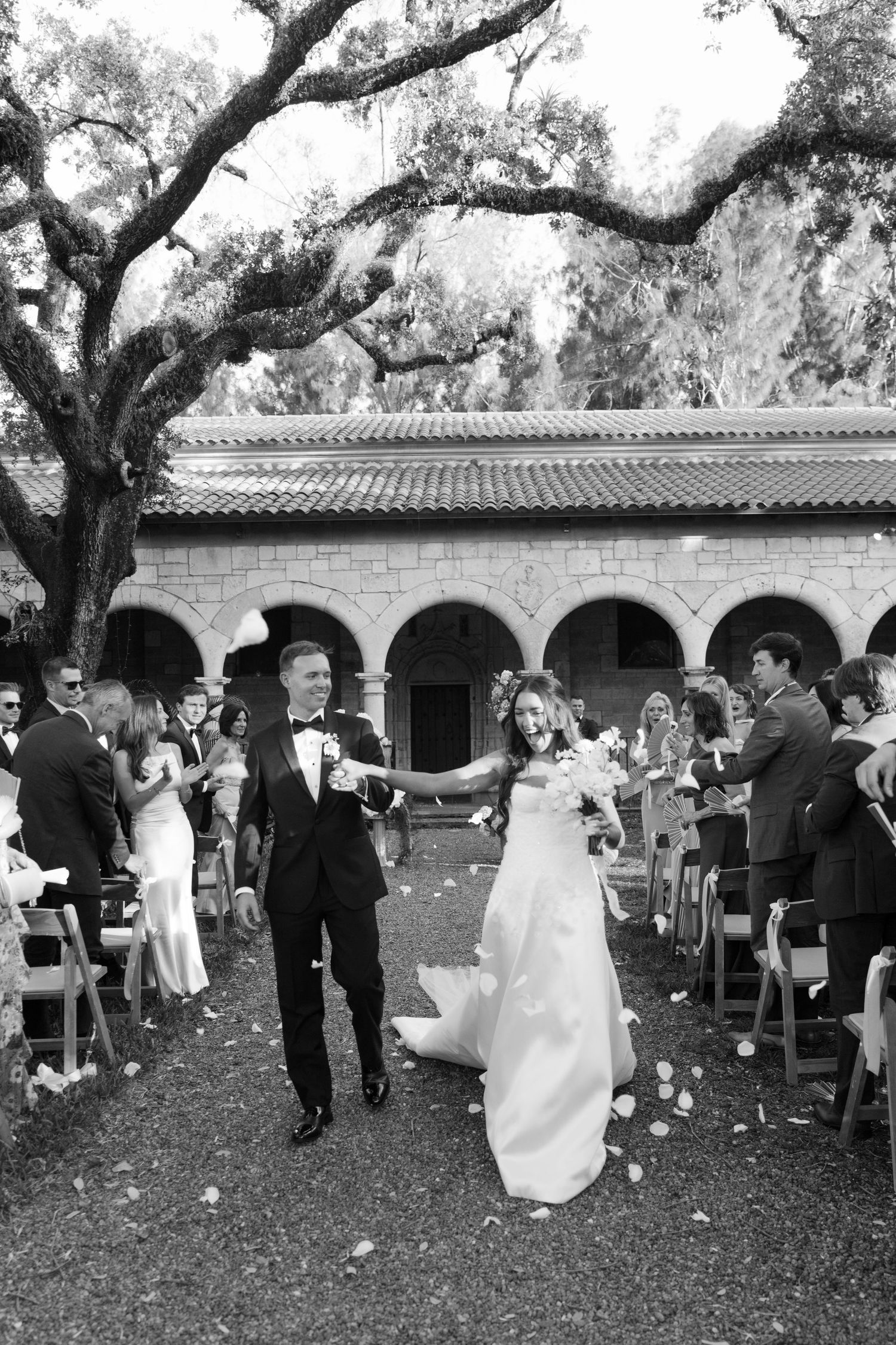 Black and white photo of a newlywed couple walking down the aisle at an outdoor wedding ceremony.
