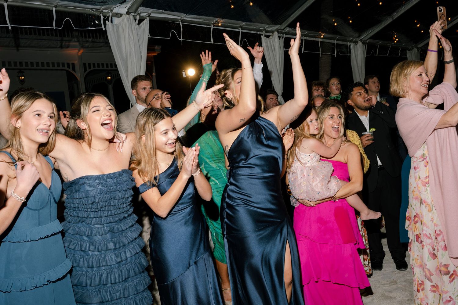 Wedding reception guests dancing and celebrating on a crowded dance floor under indoor lighting.
