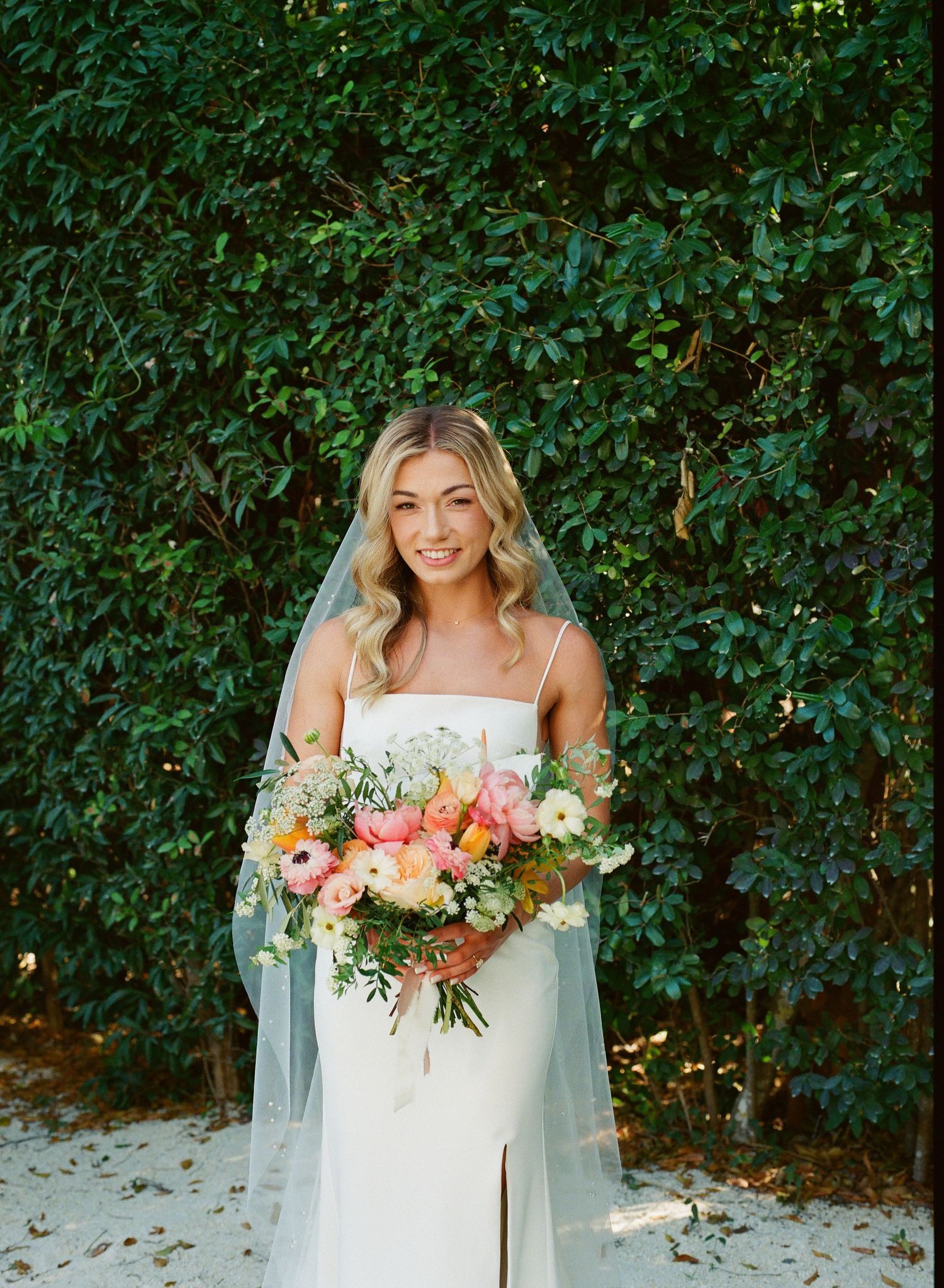 Beautiful bridal portrait against green hedge backdrop with colorful floral bouquet.