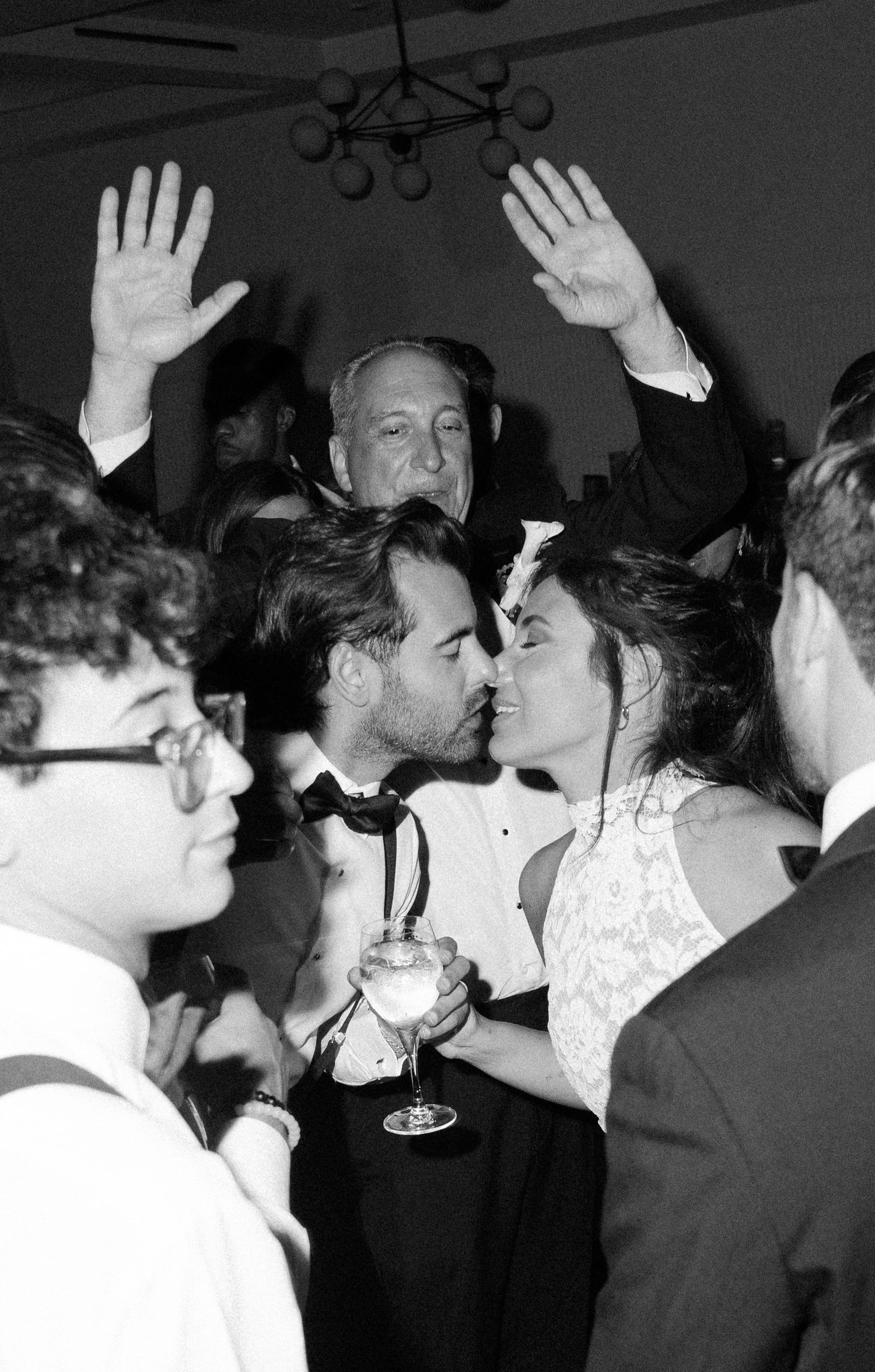 Wedding guests dancing and celebrating with raised hands on a dark dance floor at a reception party.