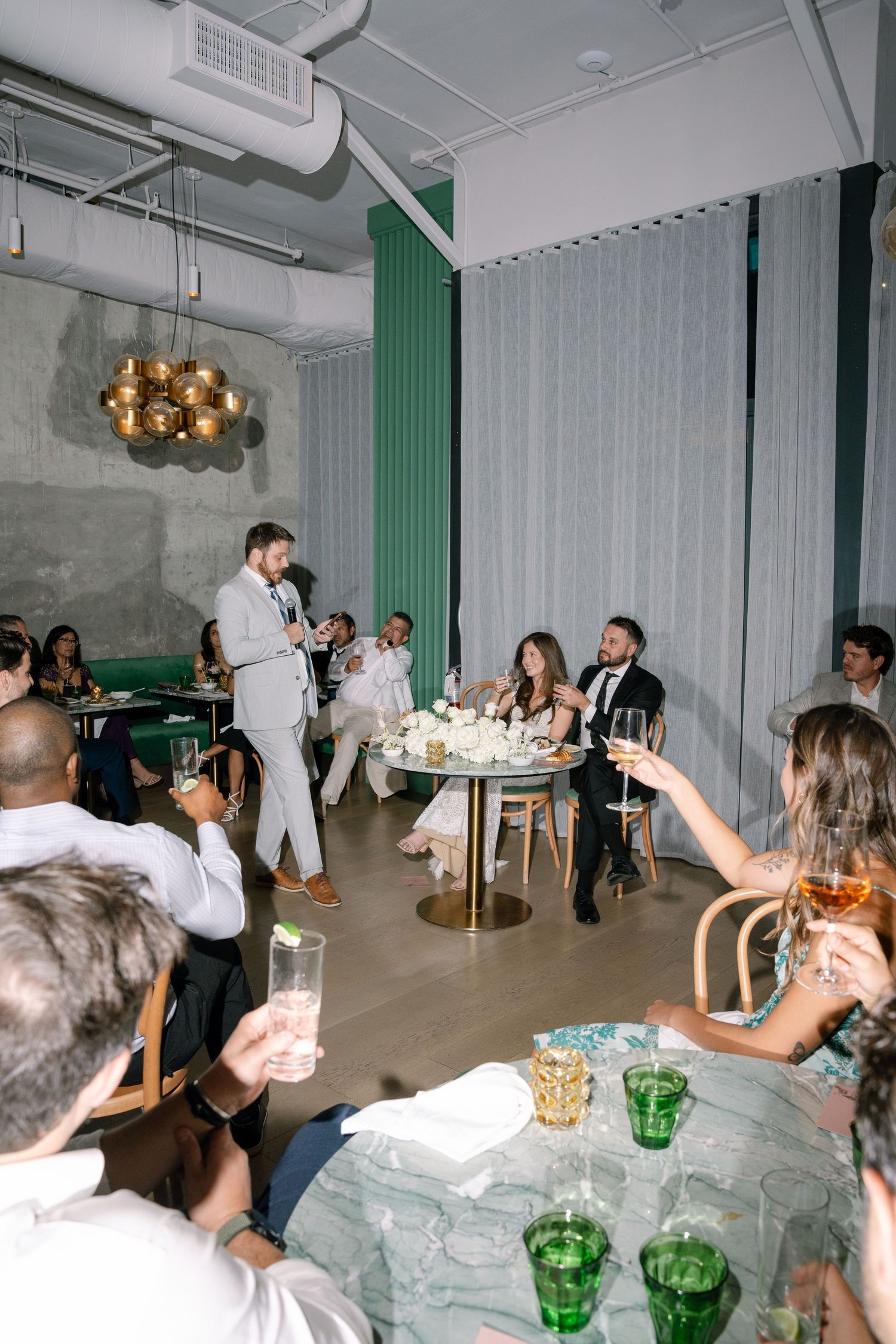 Modern reception venue with green accents features guests mingling at white tables with colorful drinks.