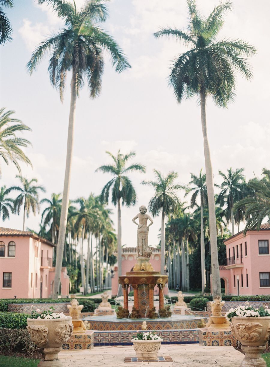 A panoramic collage of pink Mediterranean-style buildings with palm trees and ornate stone sculptures in a courtyard setting.