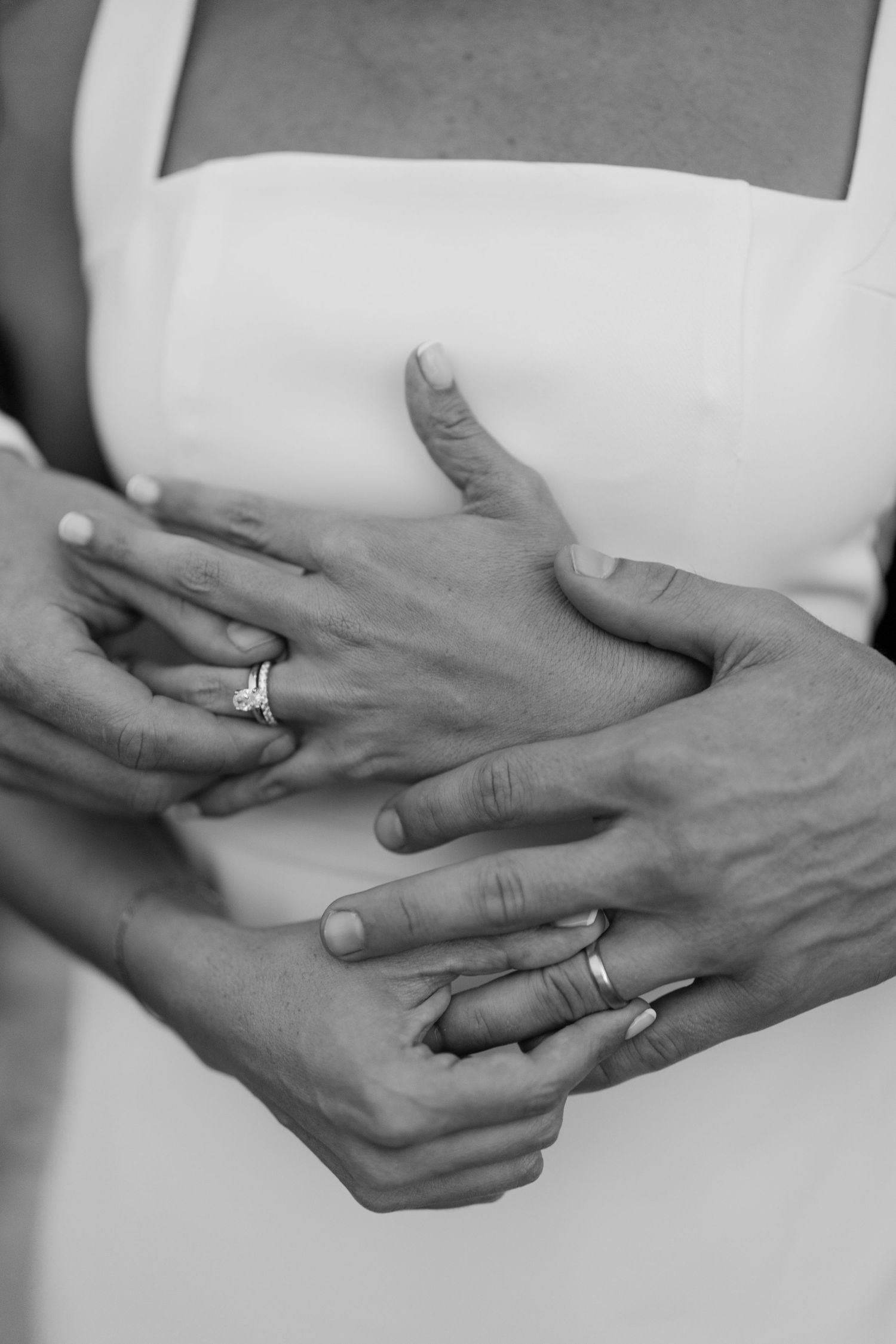 Black and white close-up of a bride and grooms hands showing their wedding and engagement rings.