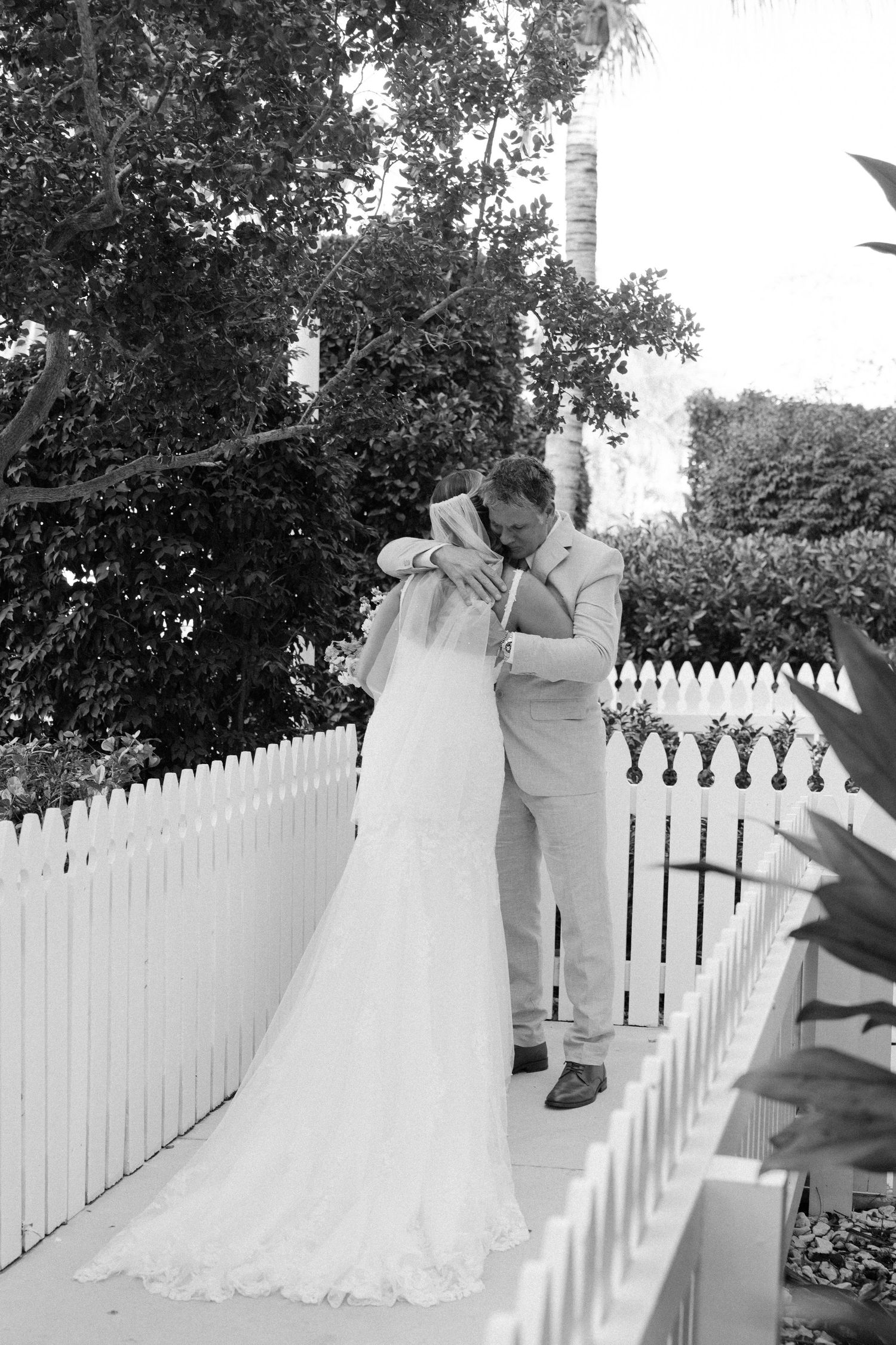 Romantic black and white wedding portrait by a white picket fence.