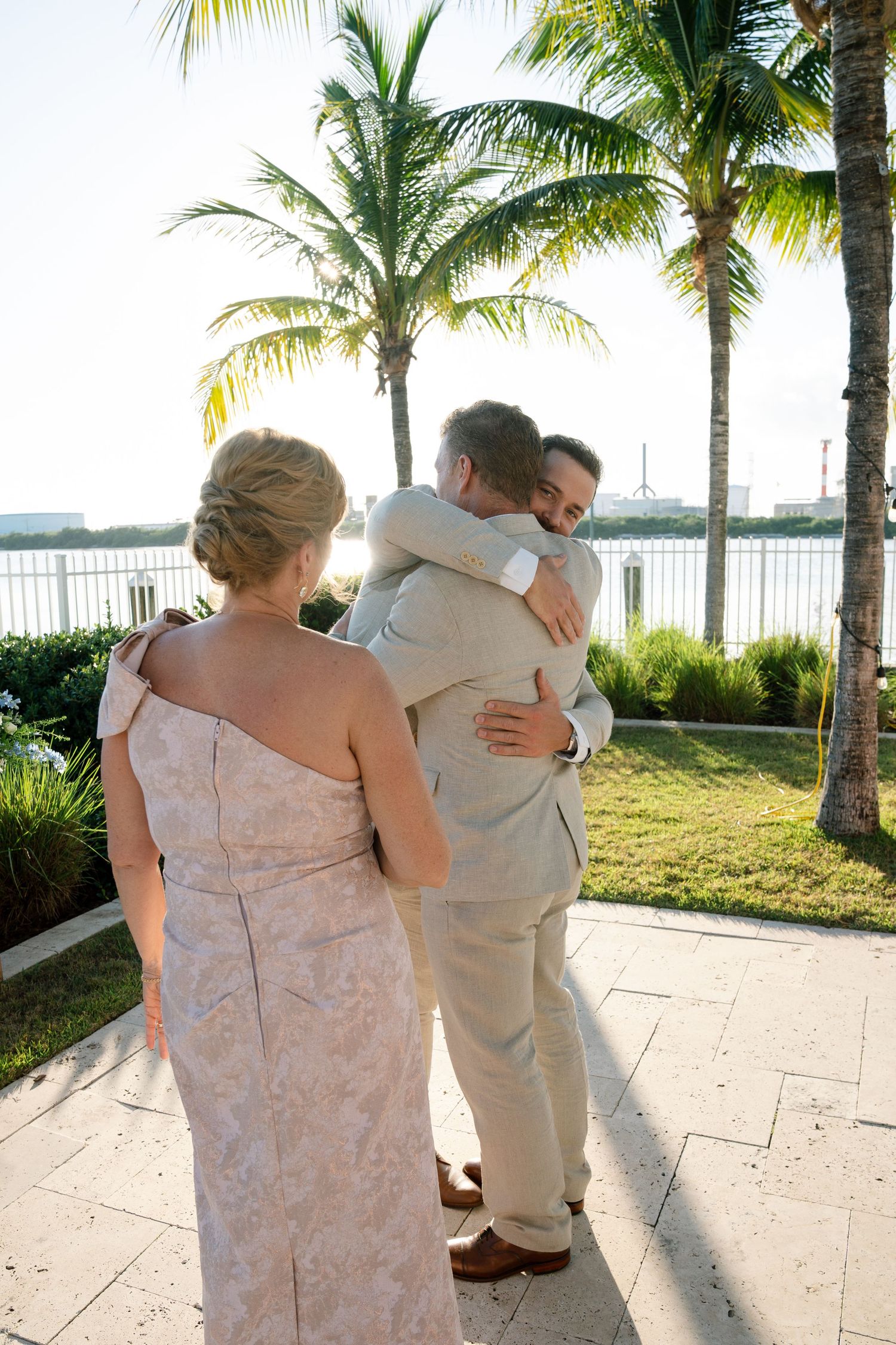 Wedding couple shares intimate moments while walking along a palm-lined pathway at sunset.