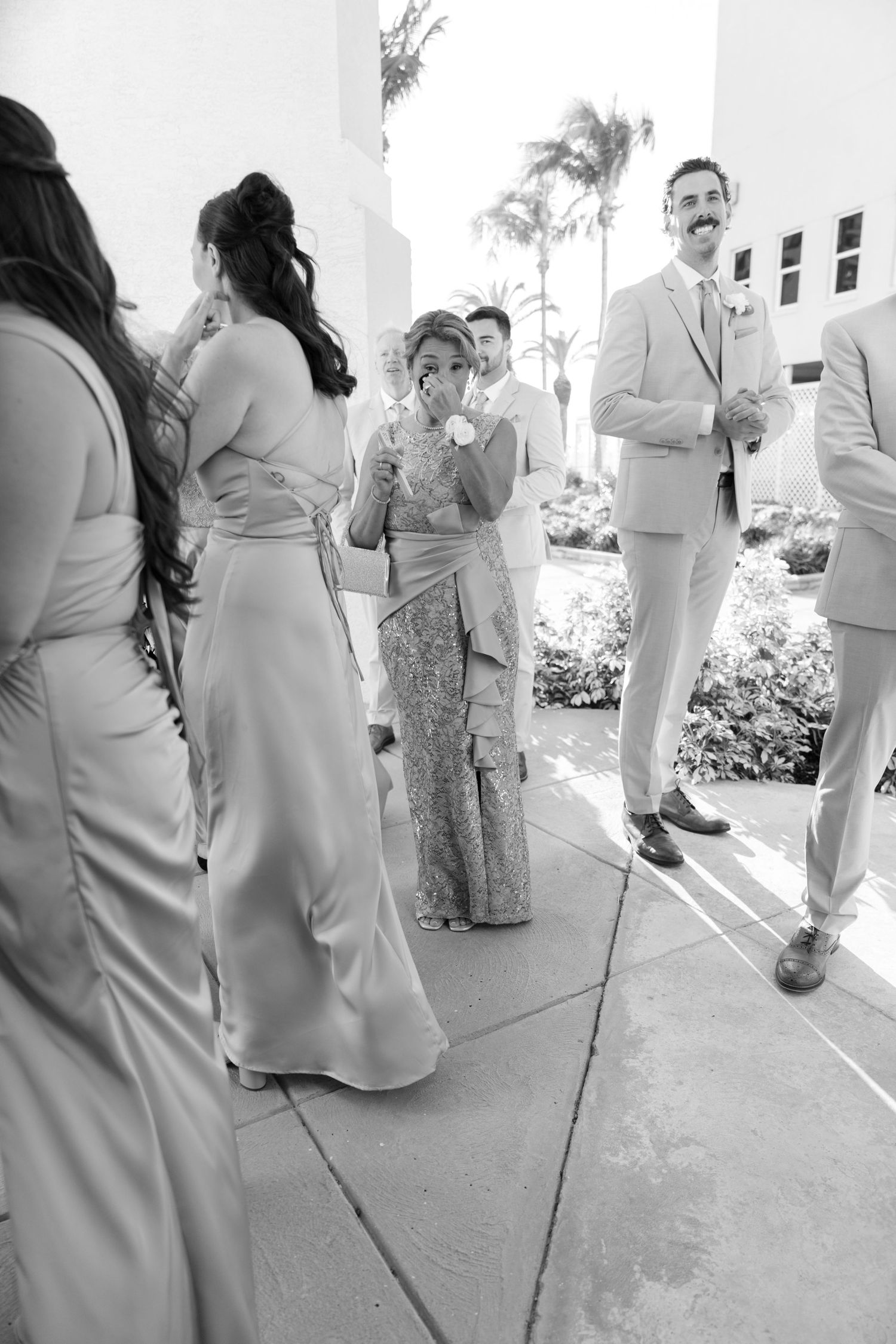 Wedding party members in light colored attire gathered outside on a sunny day.