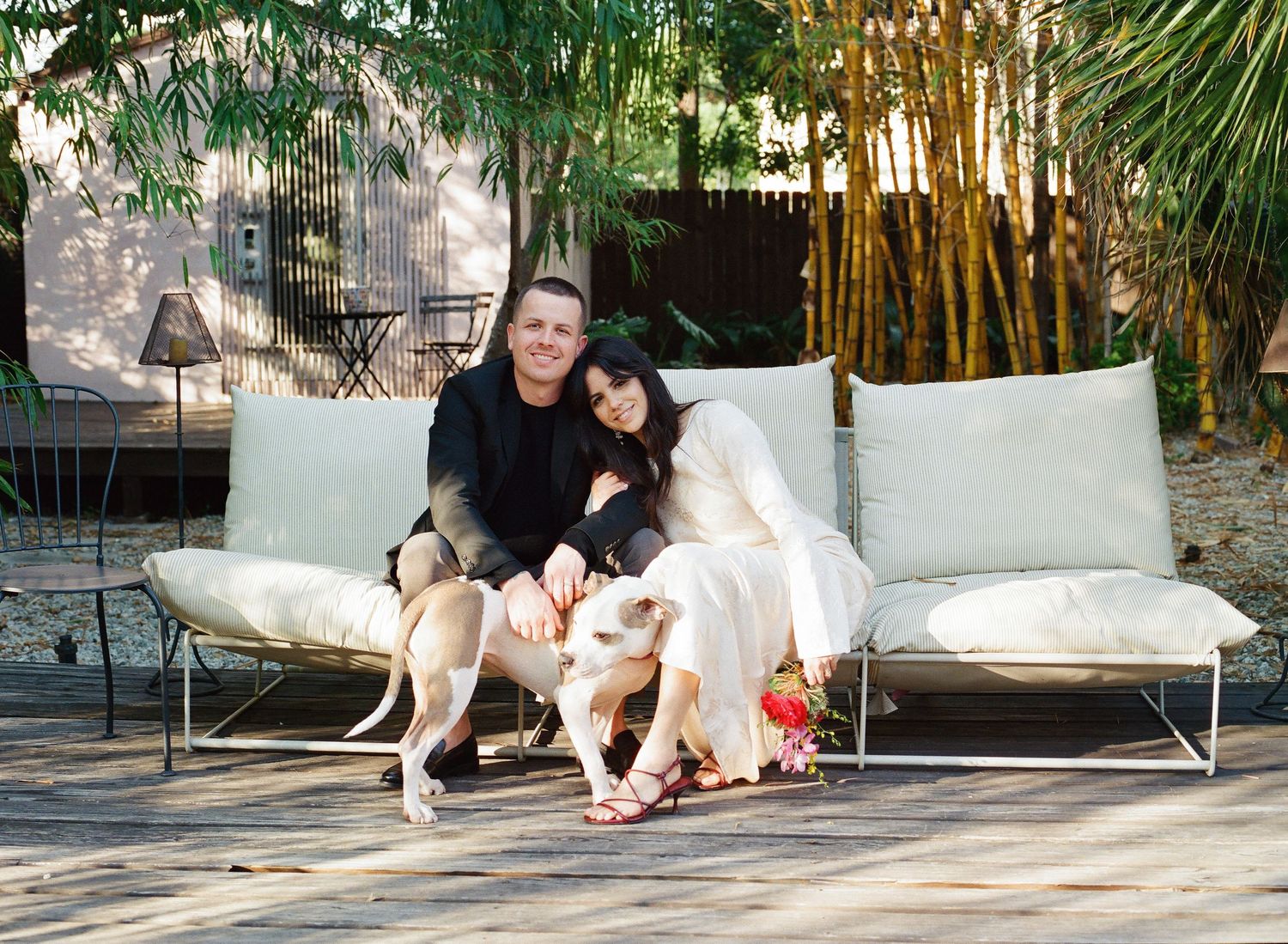 People relaxing on white outdoor furniture in a tropical garden setting with bamboo backdrop.