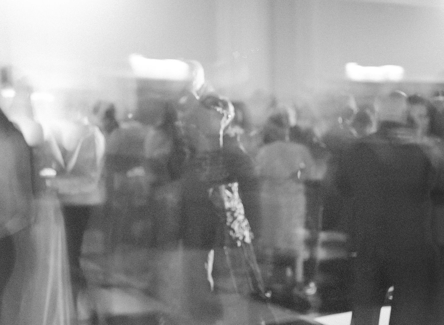 A blurred black and white photo shows silhouettes of people dancing at a reception or party.