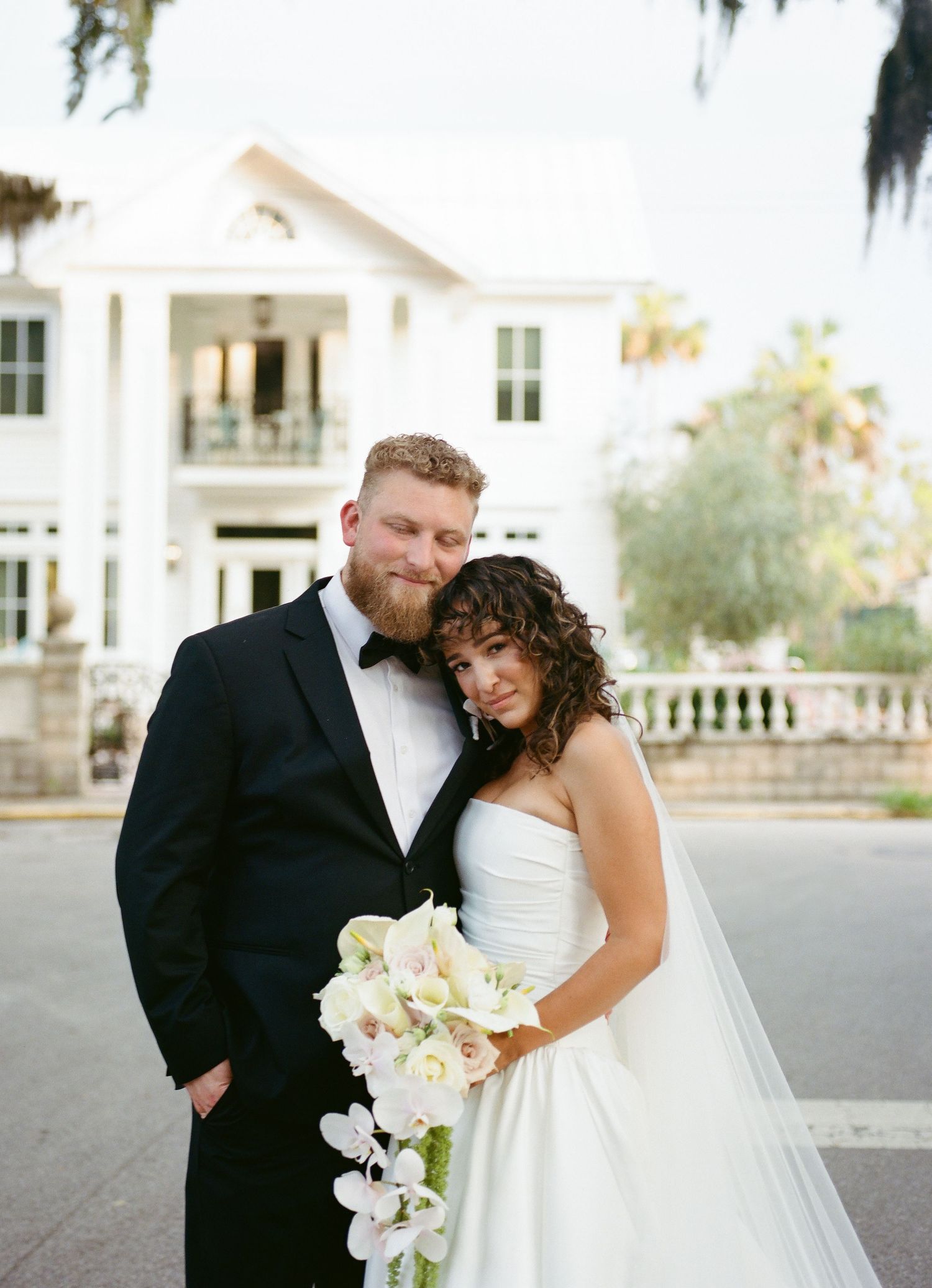 Intimate wedding portrait of couple standing close together with cascading white orchid bouquet.