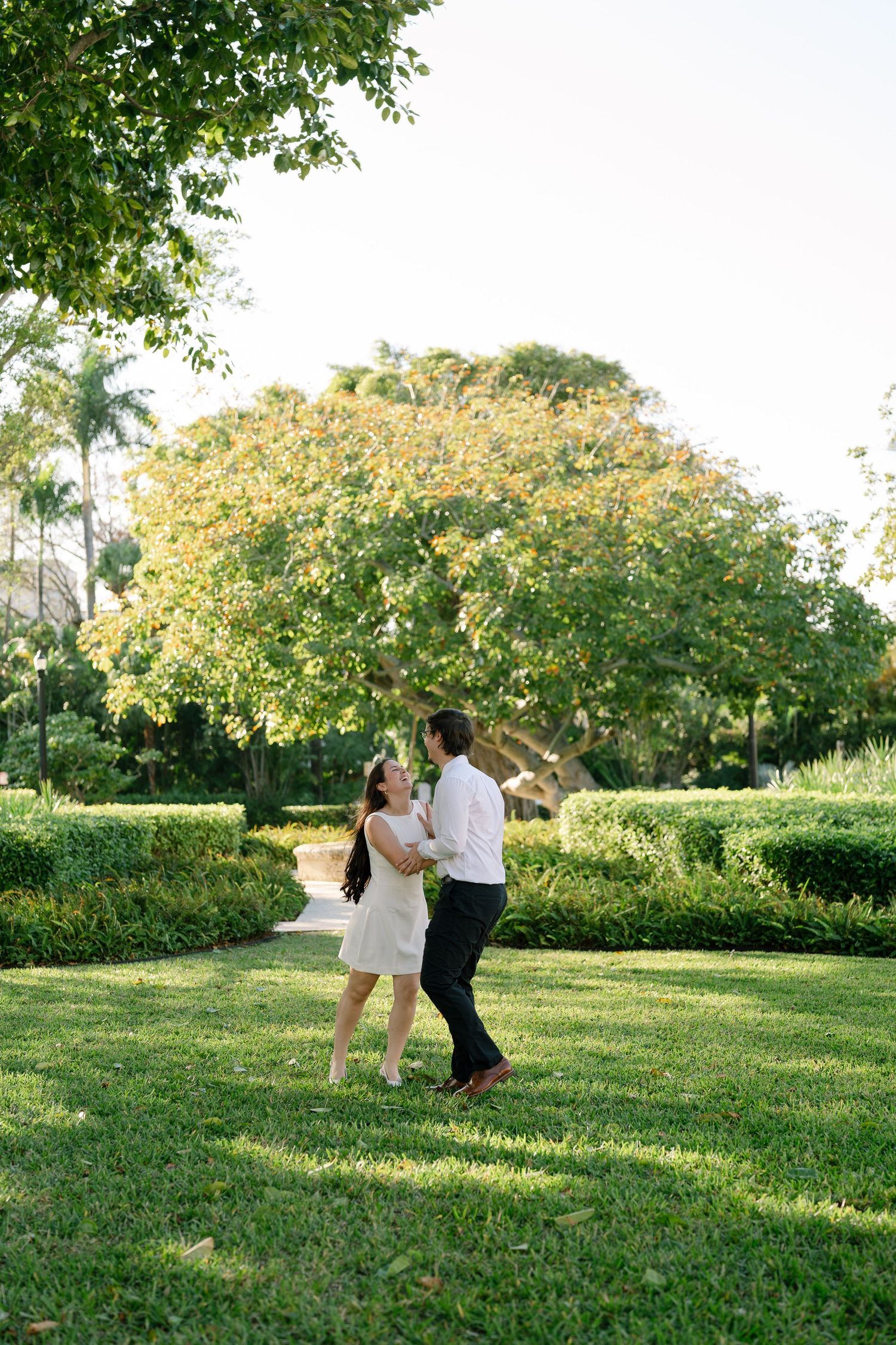 A couple dances and dips romantically on a lush green lawn surrounded by trees in a garden setting.