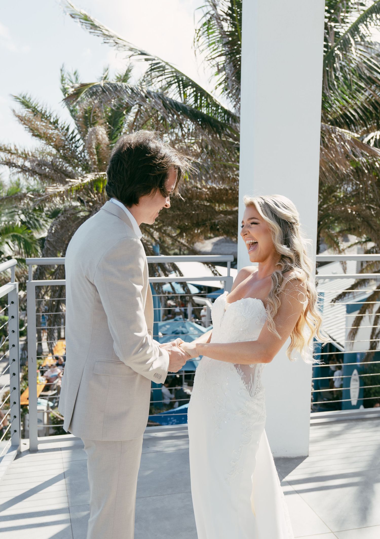 Two people share a joyful moment dancing and twirling on a white-columned patio with palm trees in the background.