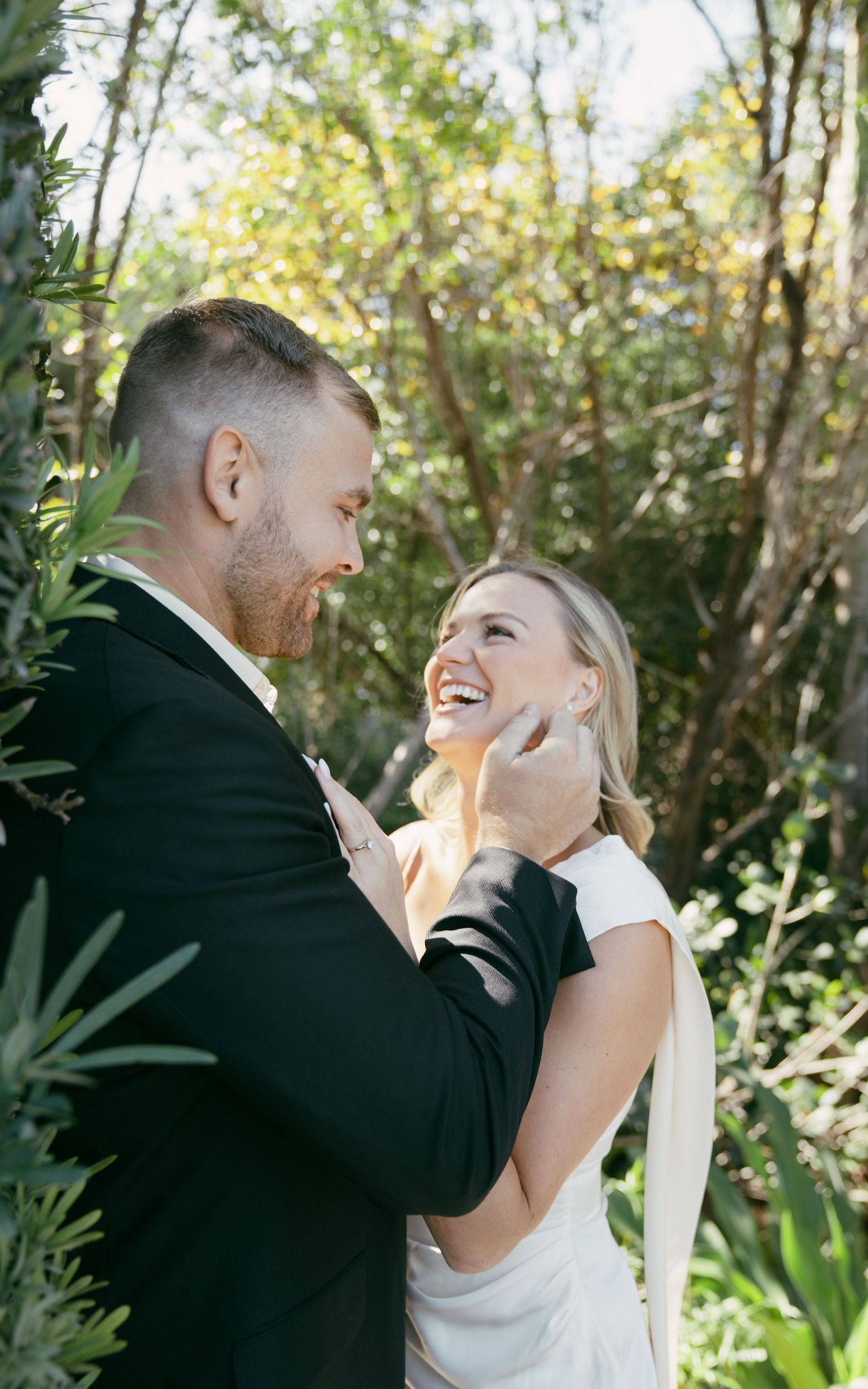 A joyful couple share an intimate moment outdoors surrounded by lush greenery during their wedding.