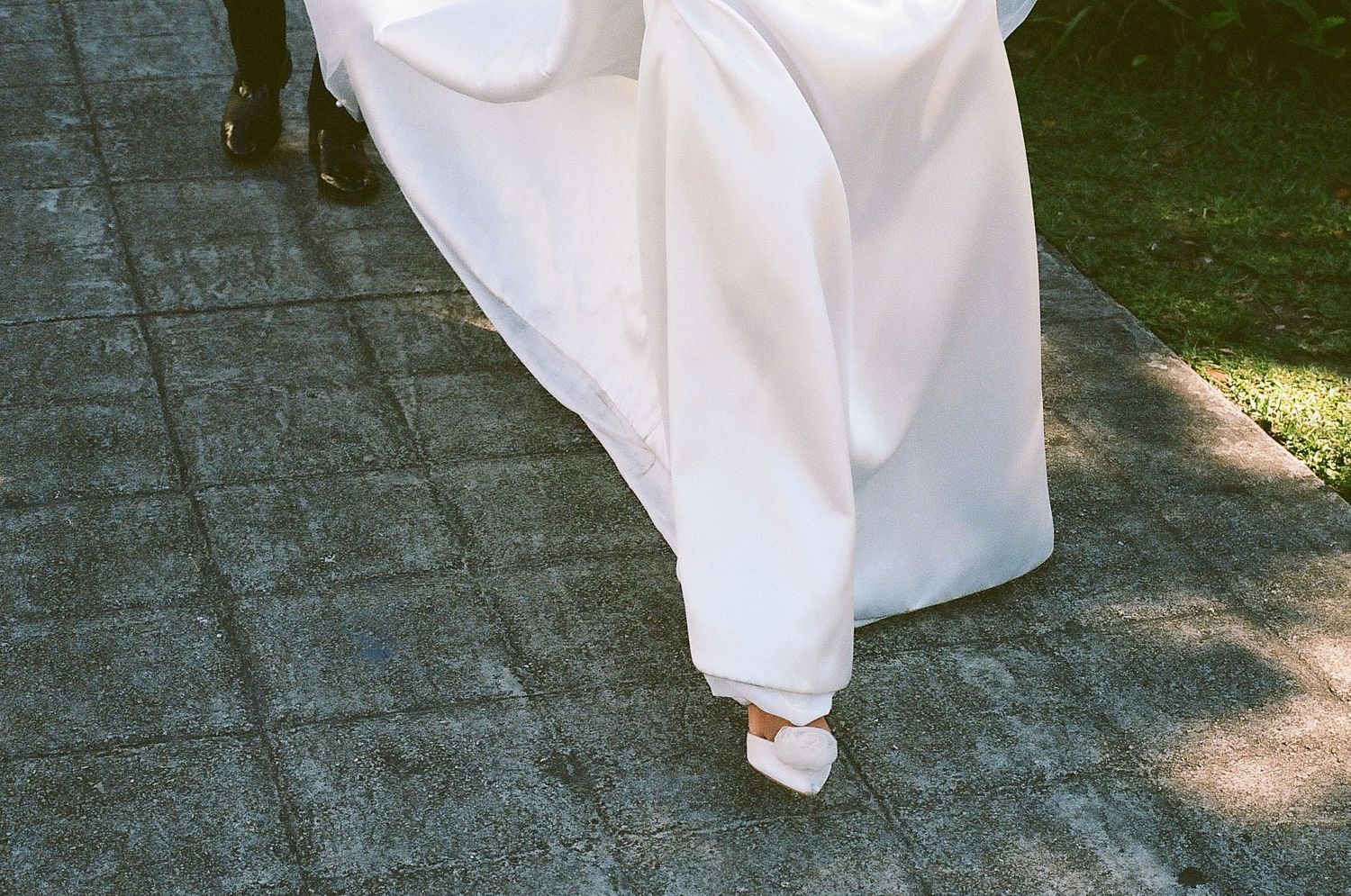 Close-up of a bride in a flowing white wedding gown and heels walking on a brick pathway.