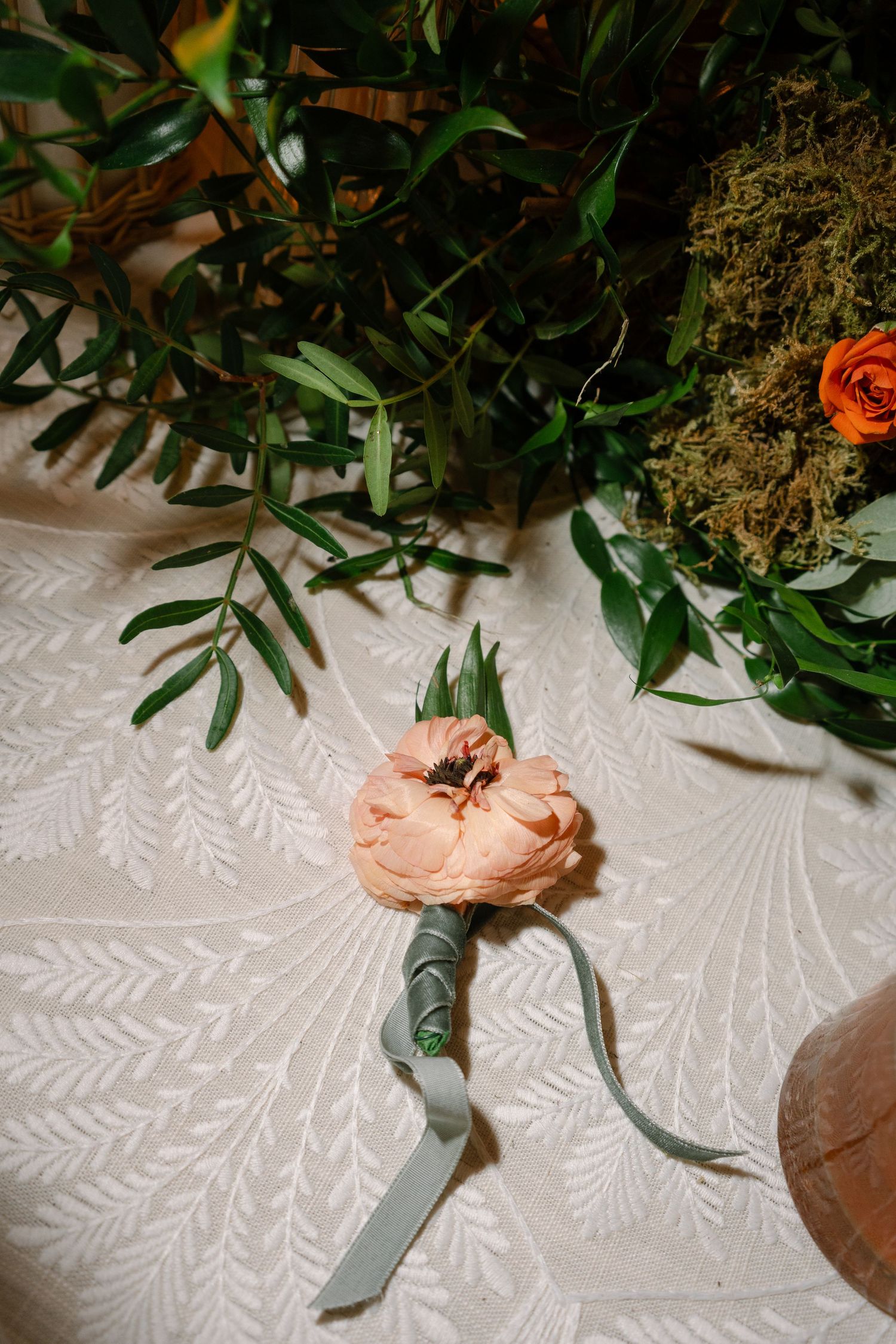 Close-up of floral table decor with peach roses and greenery on white textured tablecloth.