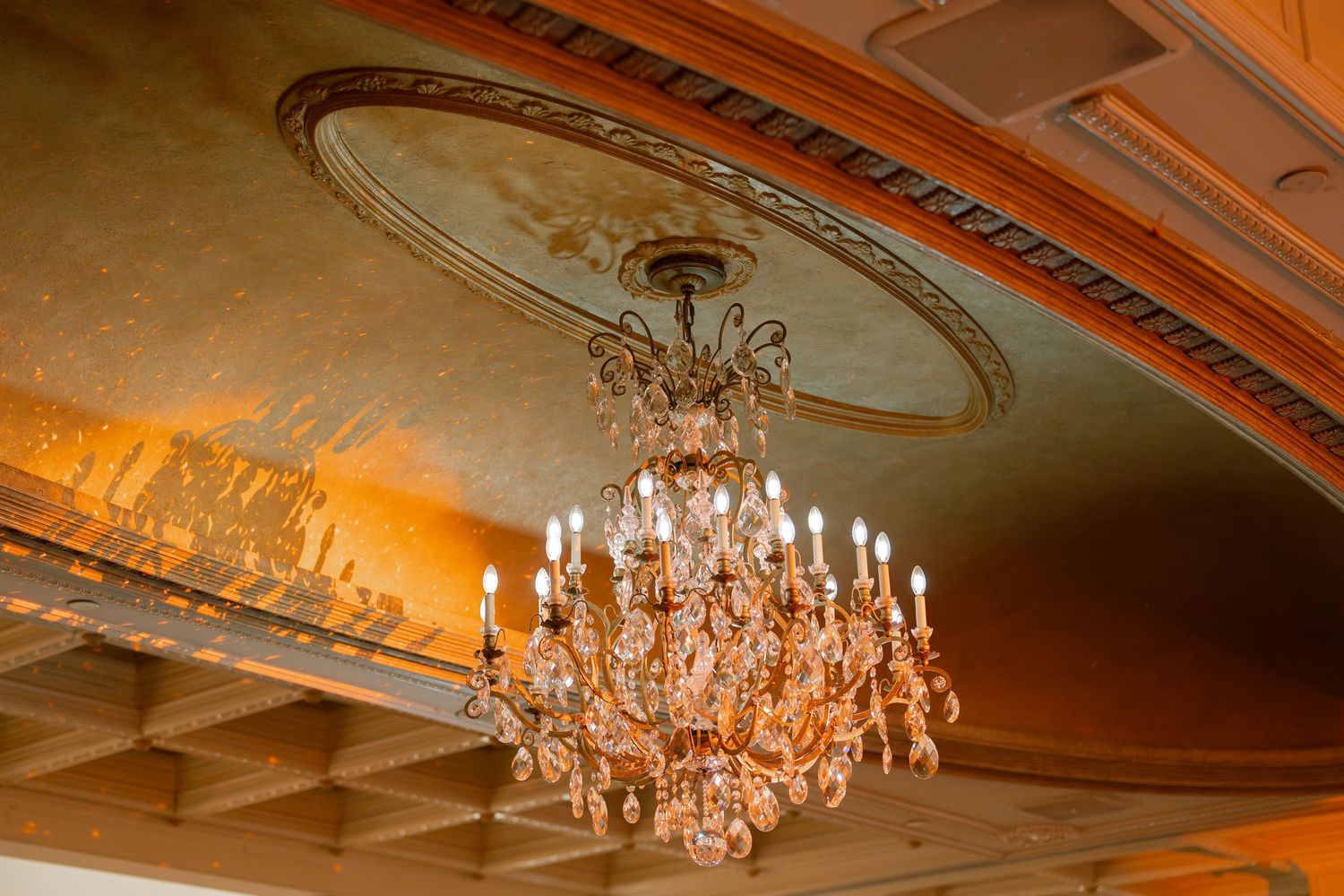 Elegant crystal chandeliers hanging from ornate ceiling with warm lighting.