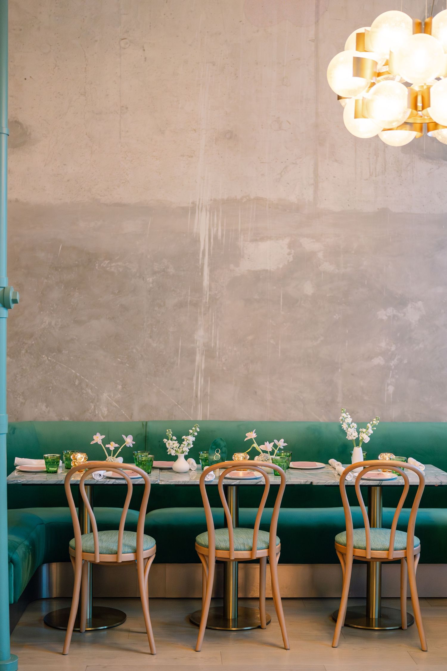 Modern restaurant interior with teal banquettes and wooden chairs arranged along a minimalist wall.