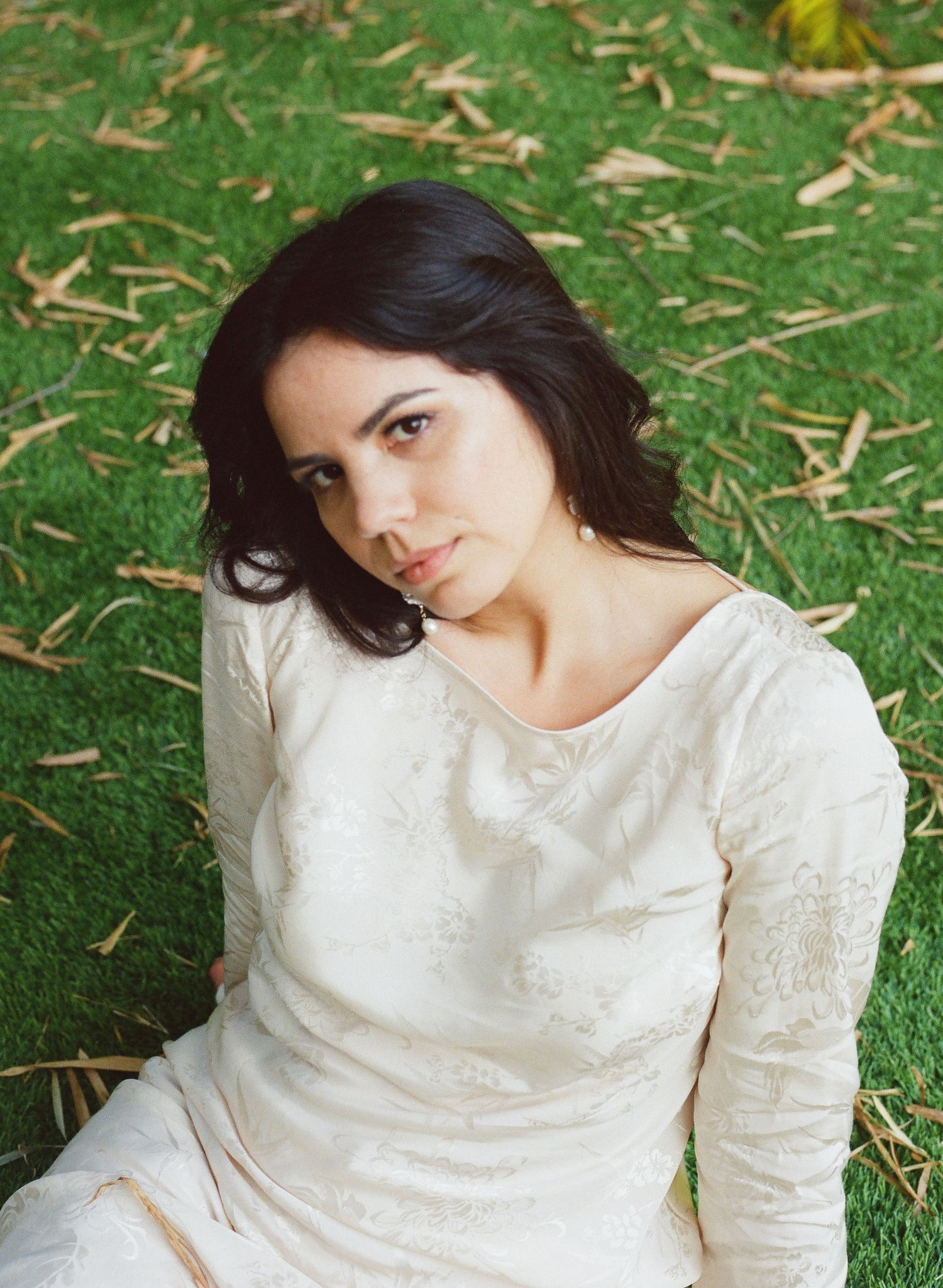 Woman in white lace dress sitting on grass with autumn leaves scattered around.