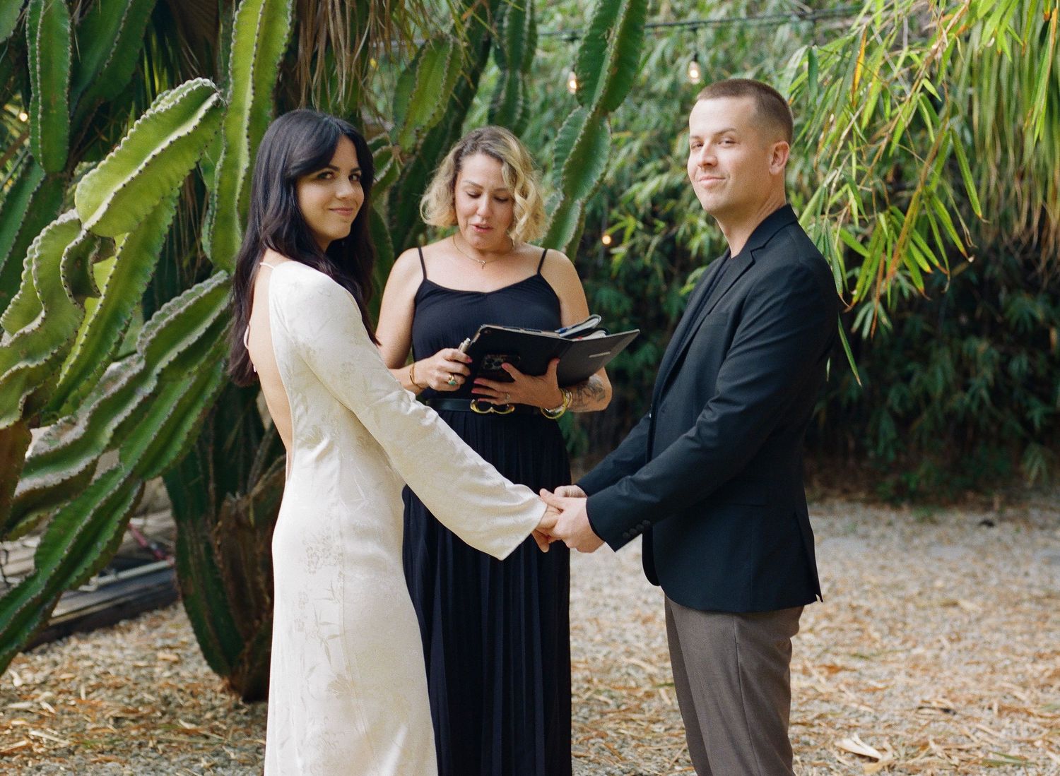 Wedding ceremony taking place in lush tropical garden with officiant and couple.