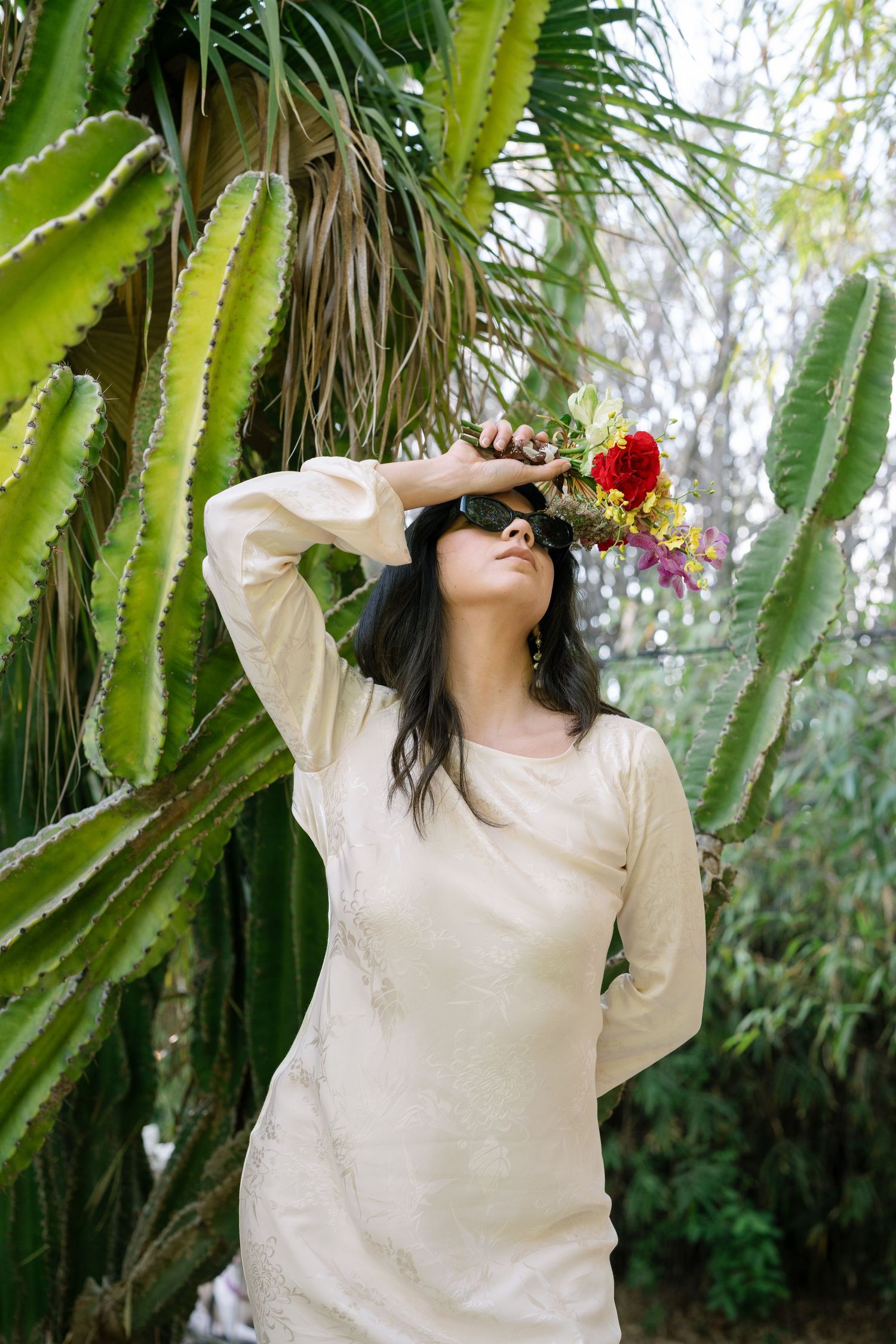 A person in a cream-colored sweater dances expressively in front of tall cactus plants.