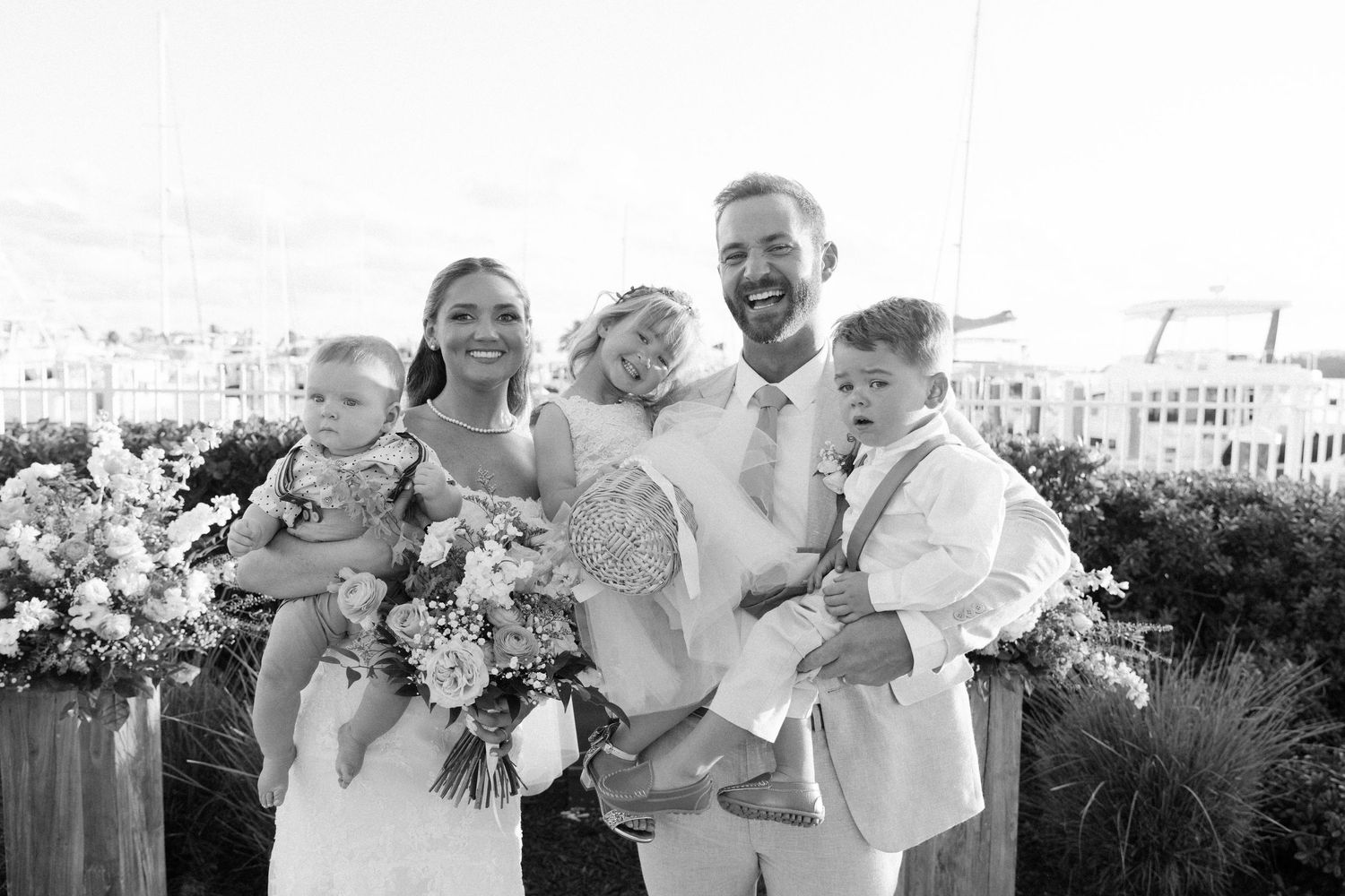 Wedding party laughs together while holding floral bouquets outdoors.