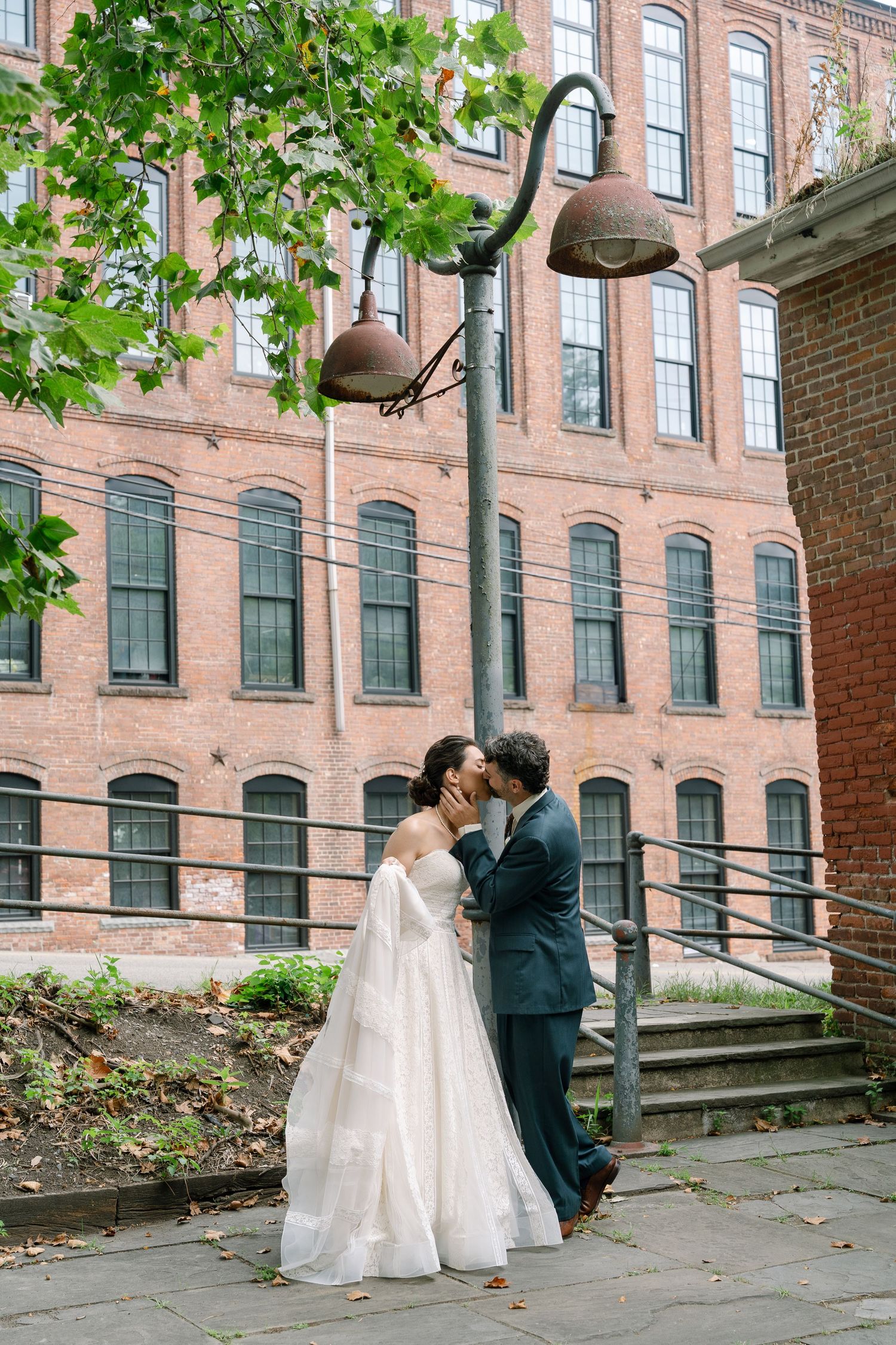 Couple sharing a romantic moment in front of a historic brick building with lush greenery.