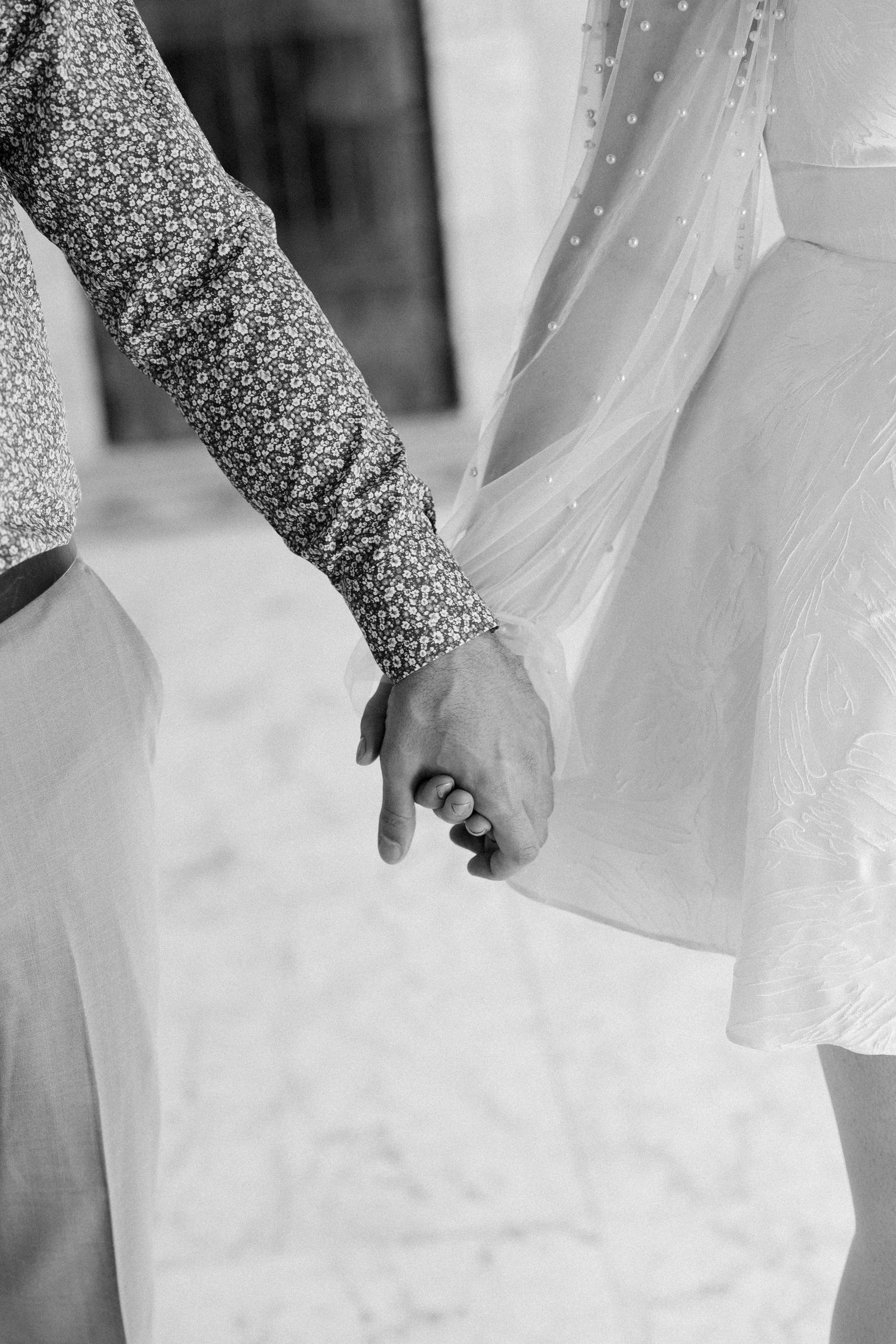 Black and white close-up of two people holding hands, one wearing a sparkly sleeve.