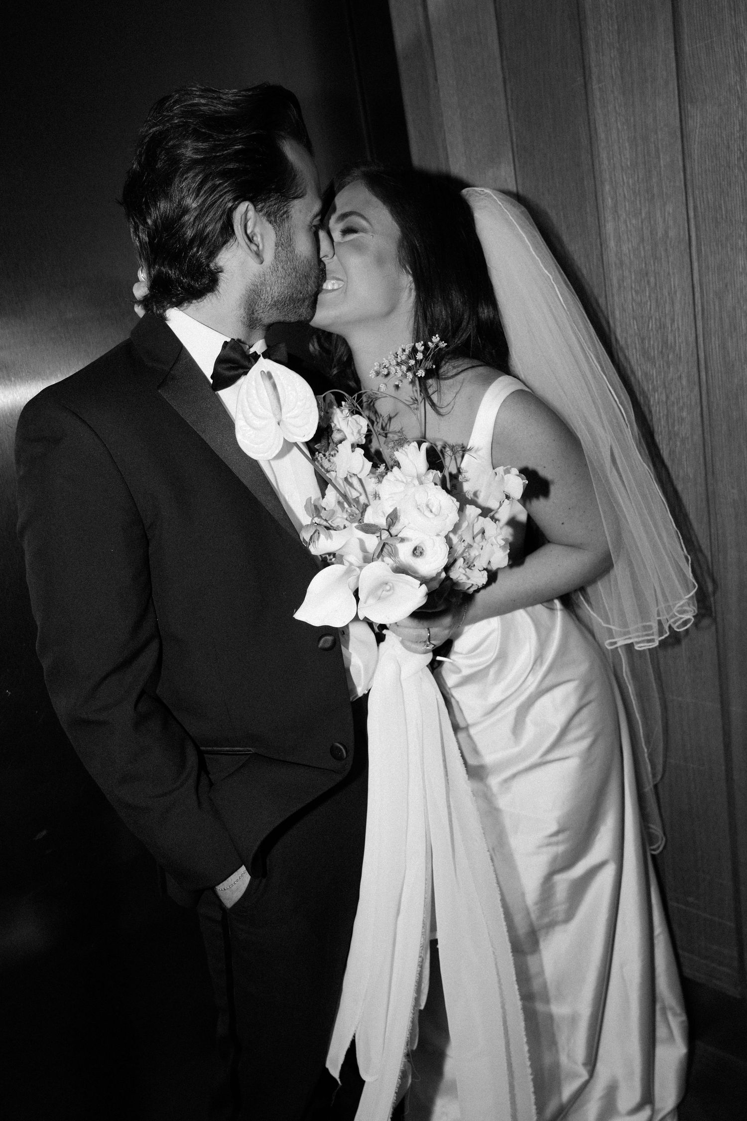 Black and white wedding photos showing romantic kiss between newlyweds with bride in white dress and flowing veil.