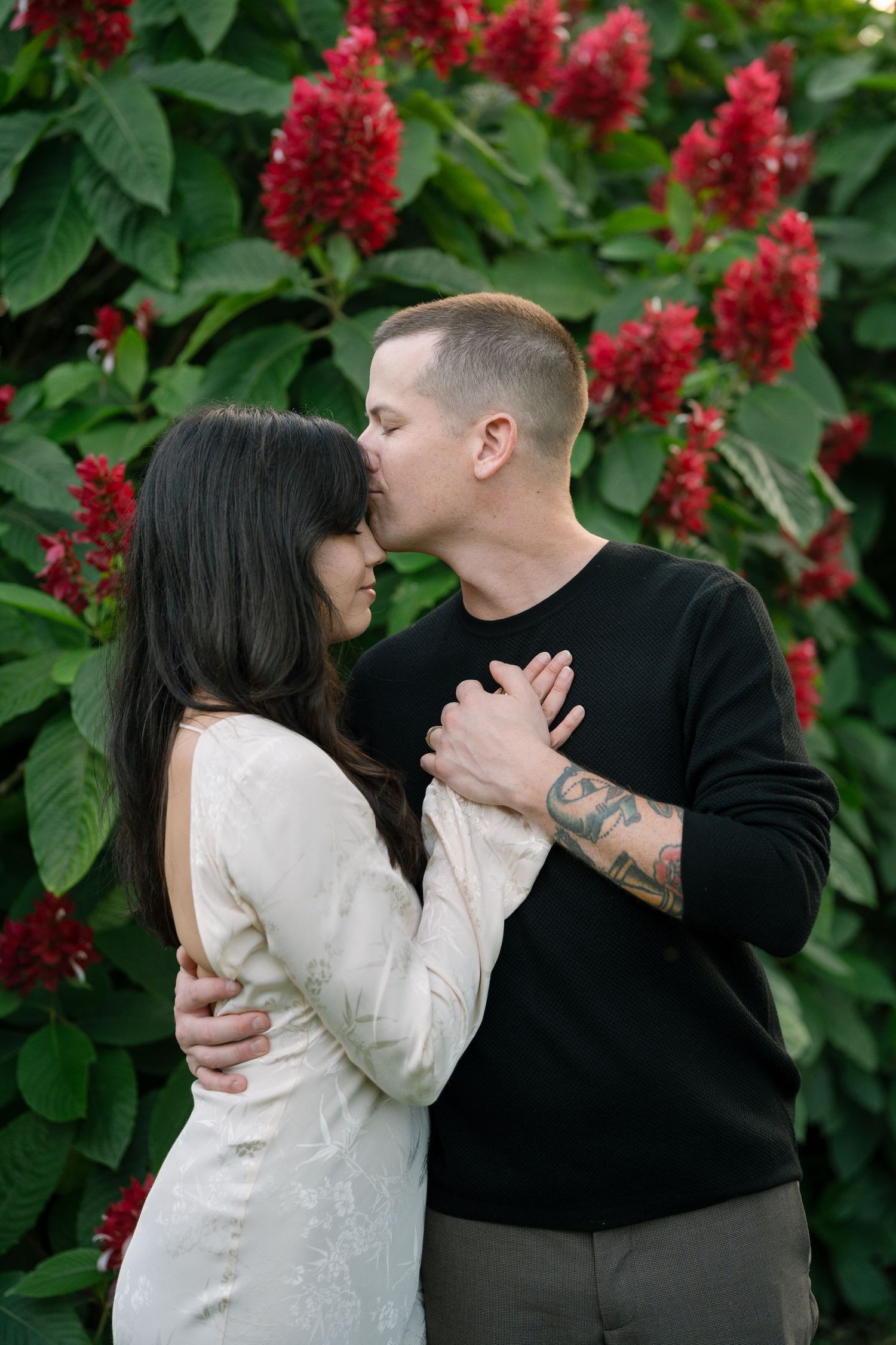 A romantic moment captured against vibrant red flowering bushes in a garden setting.