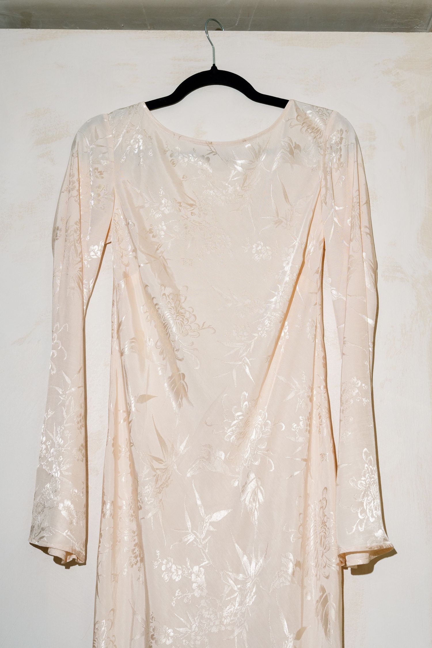 Cream-colored vintage dress with sequins hanging on black hanger against white wall.