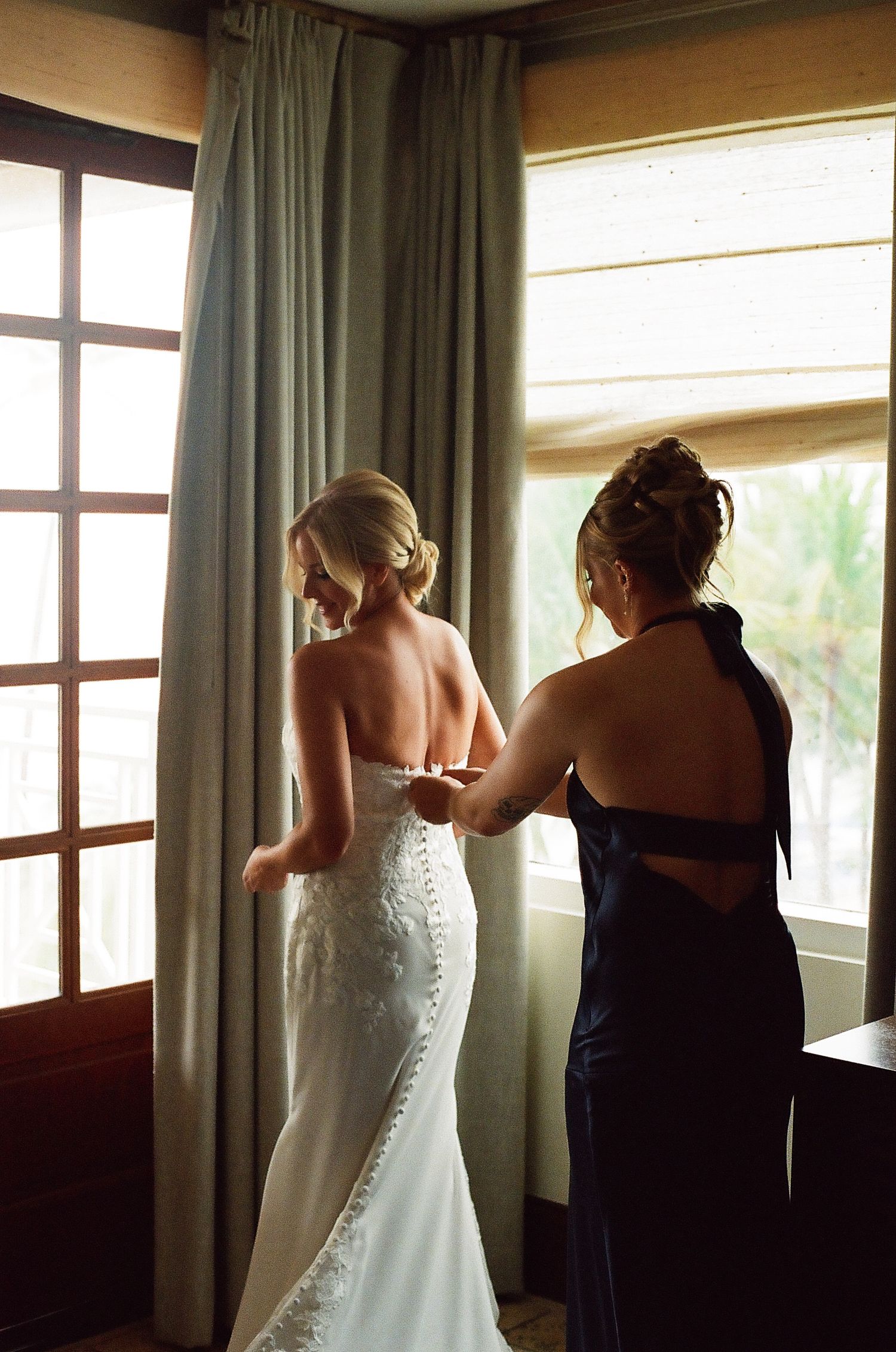 Wedding preparation scene by window with flowing white dress and navy blue accents in natural light.