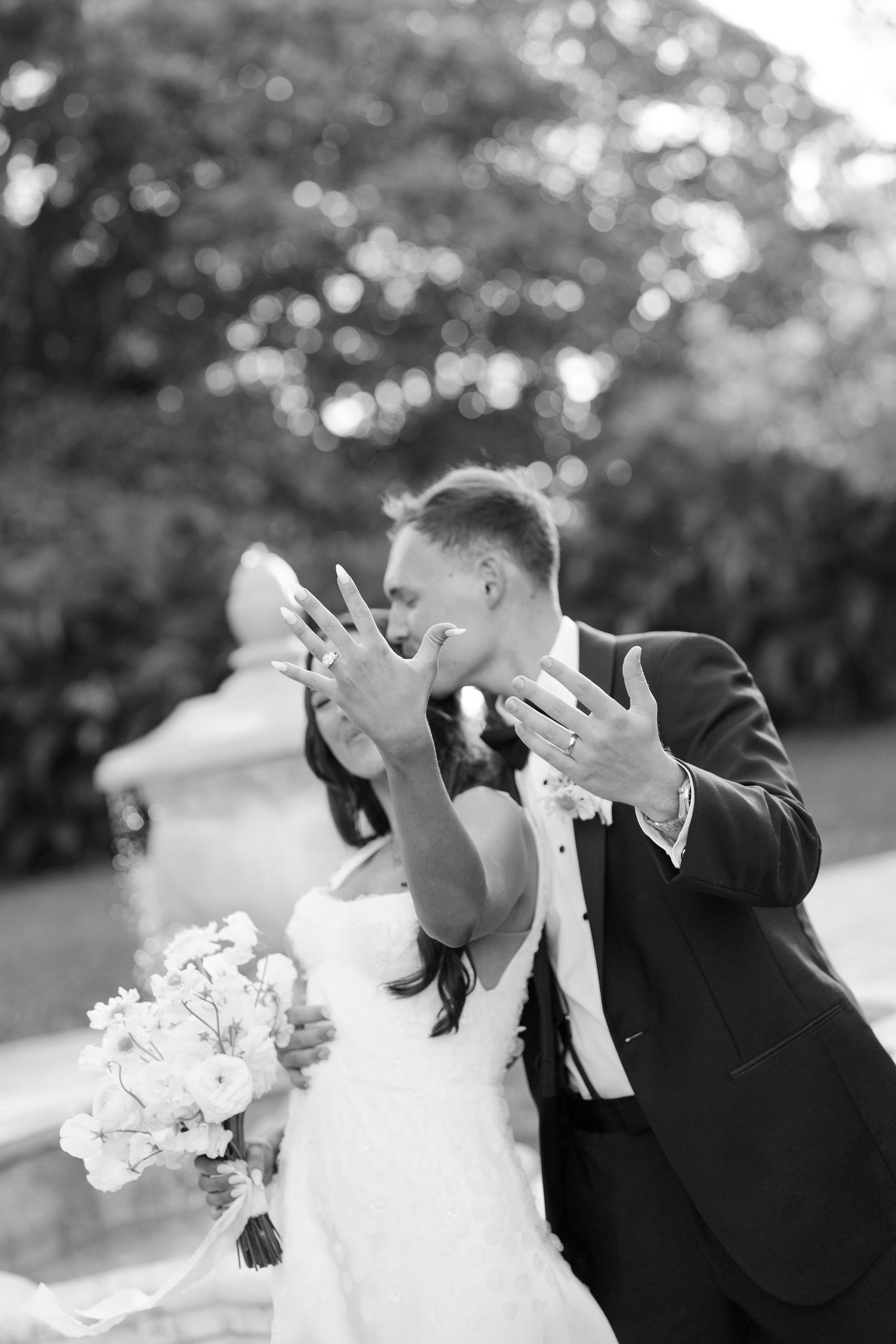 A black and white photo of a bride and groom kissing while showing off their wedding rings.