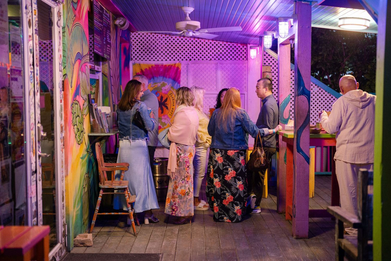 People gather in a purple-lit hallway with colorful decorations and artwork displays during an indoor event.