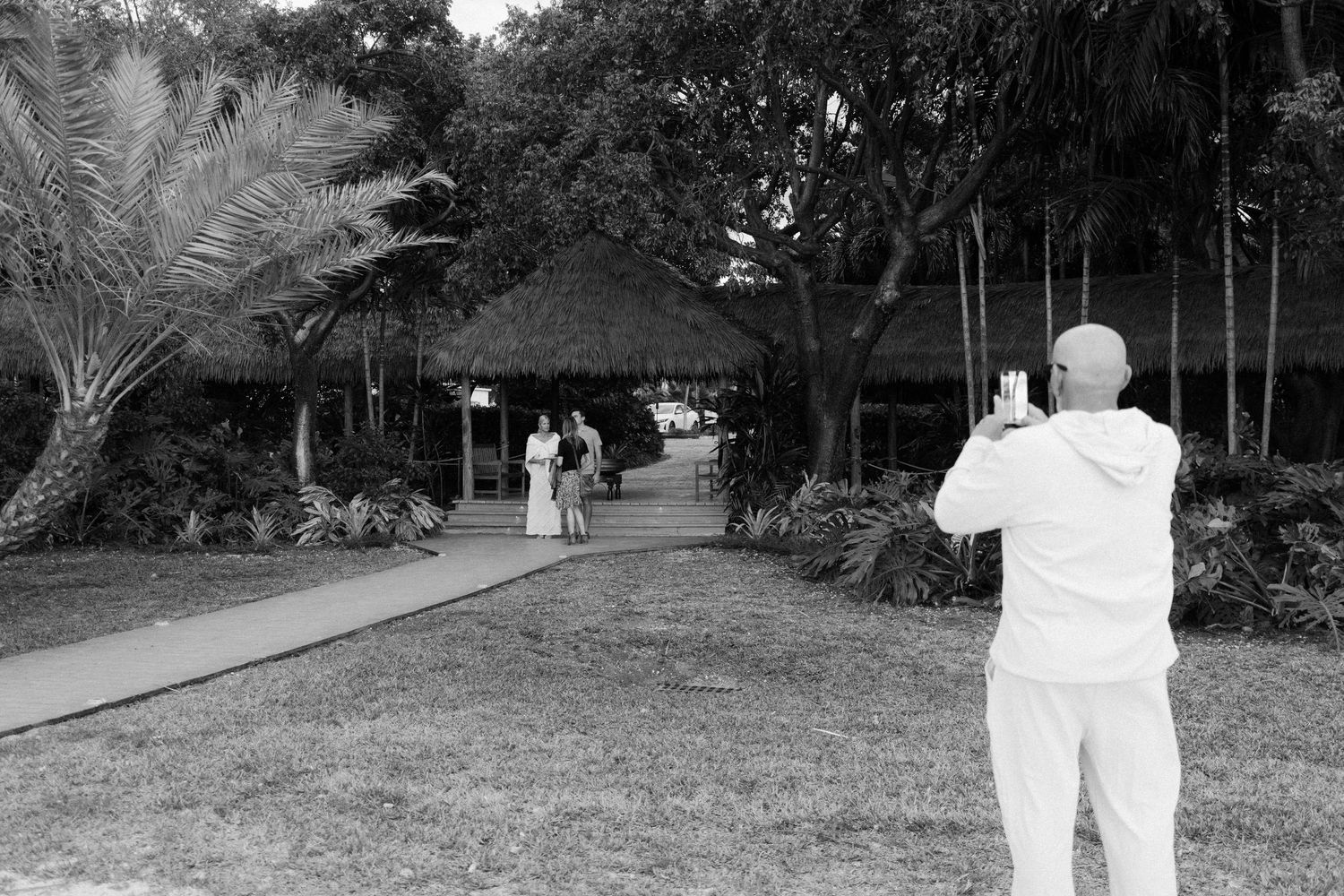 A person in white protective gear sprays disinfectant on outdoor surfaces during a sanitization procedure.