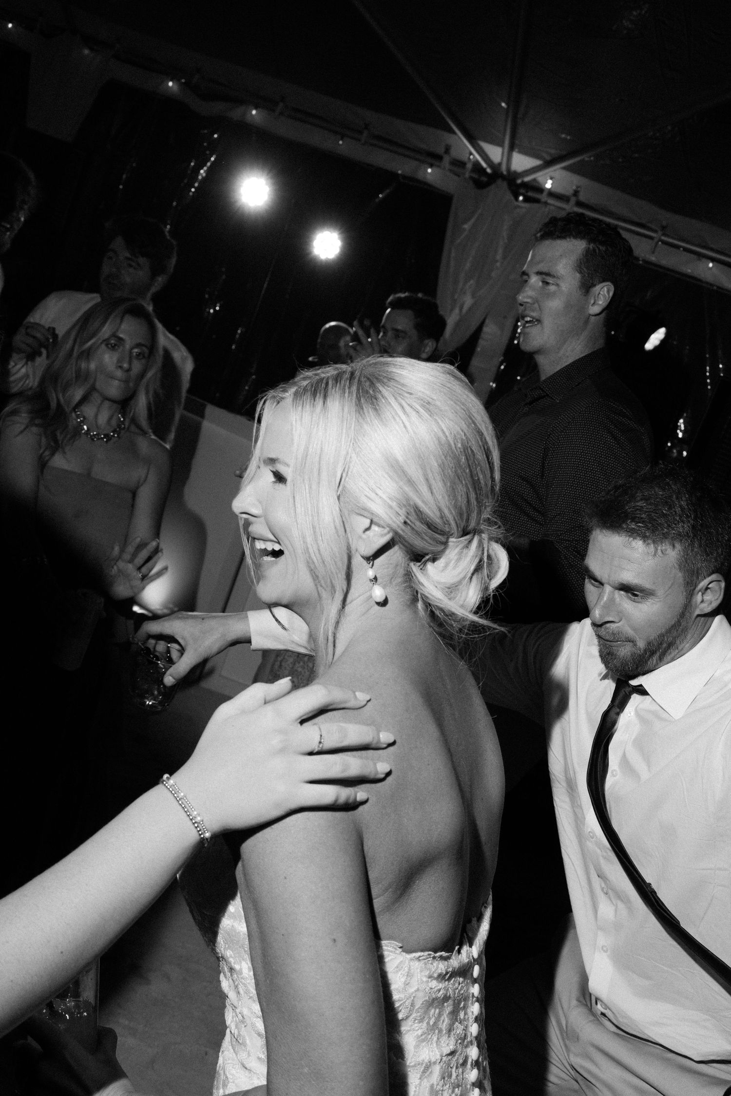 Black and white photo of people dancing and celebrating at a party with overhead lighting.