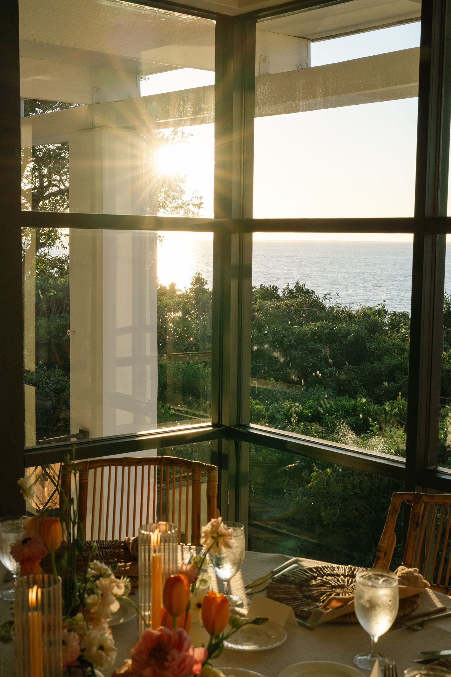 Elegant wedding reception setup in a sunlit glass-enclosed porch overlooking scenic views.