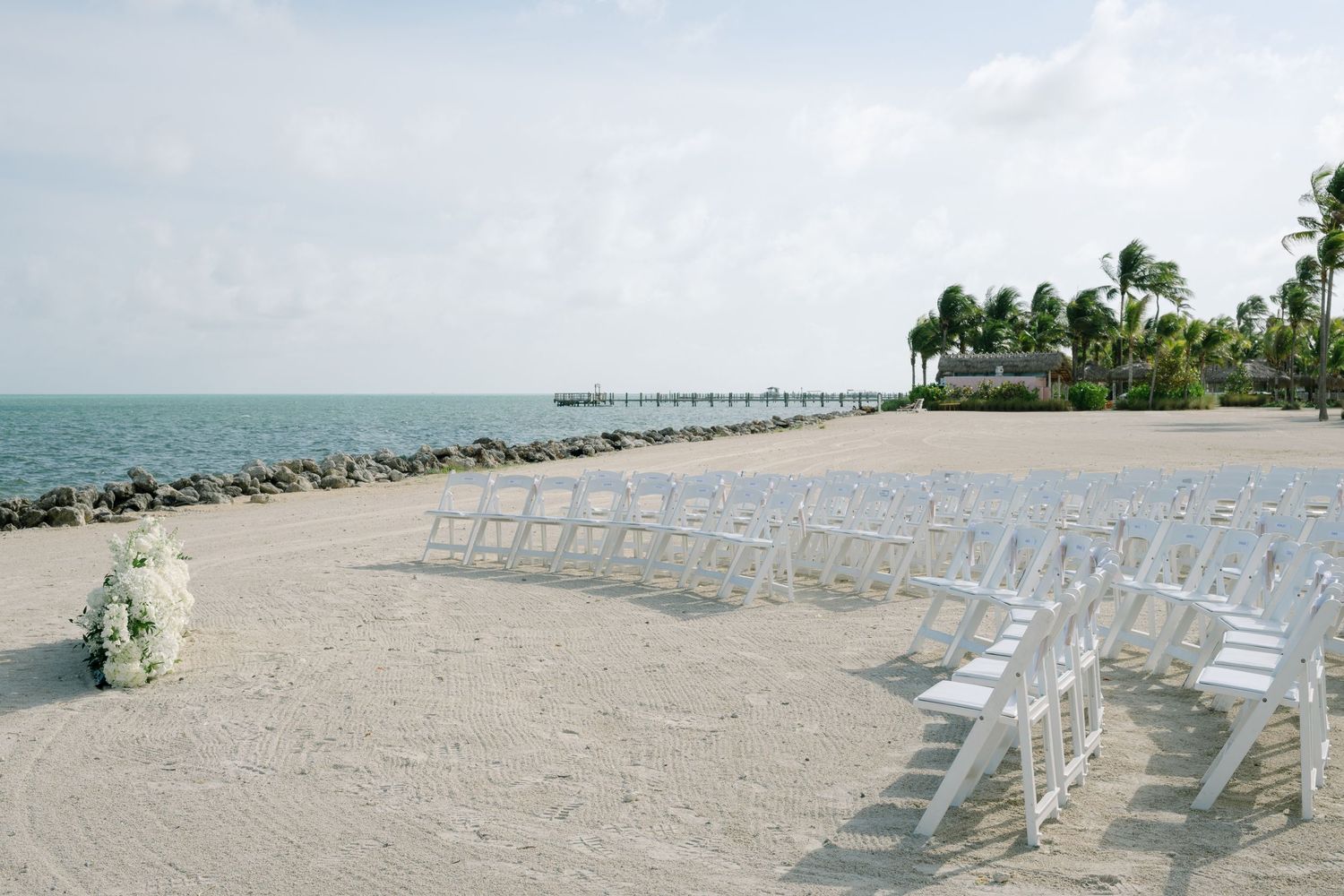 White chairs arranged on a sandy beach for an outdoor wedding ceremony with ocean views.