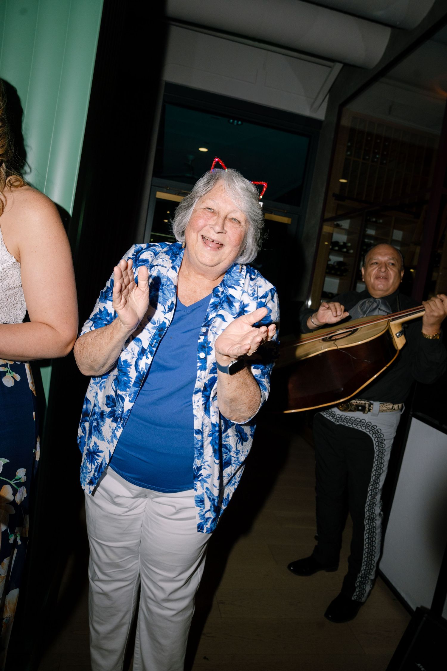 Elderly woman in blue and white floral shirt dancing energetically at an indoor event.