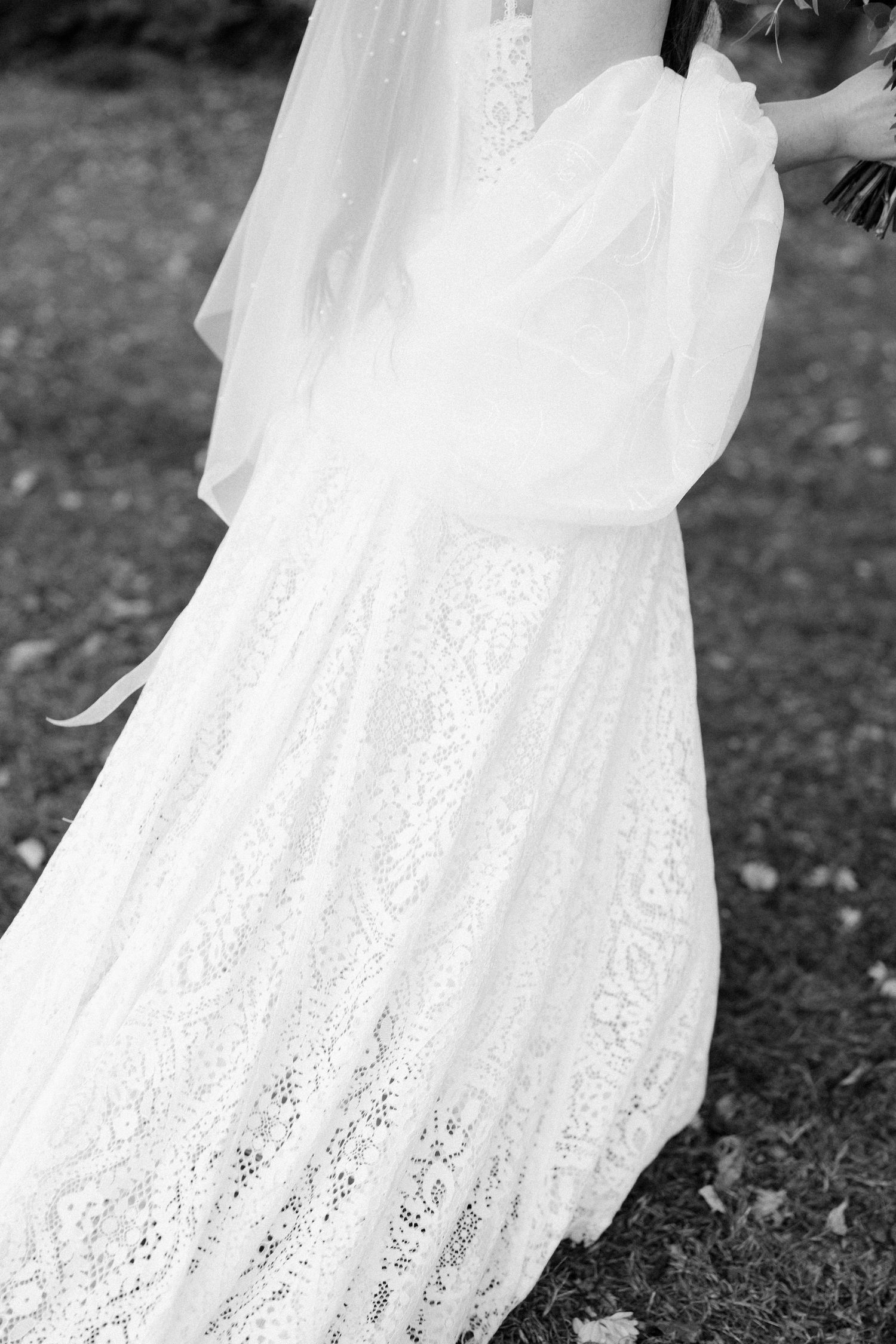 Close-up detail of a white lace wedding dress flowing in the breeze against a dark background.