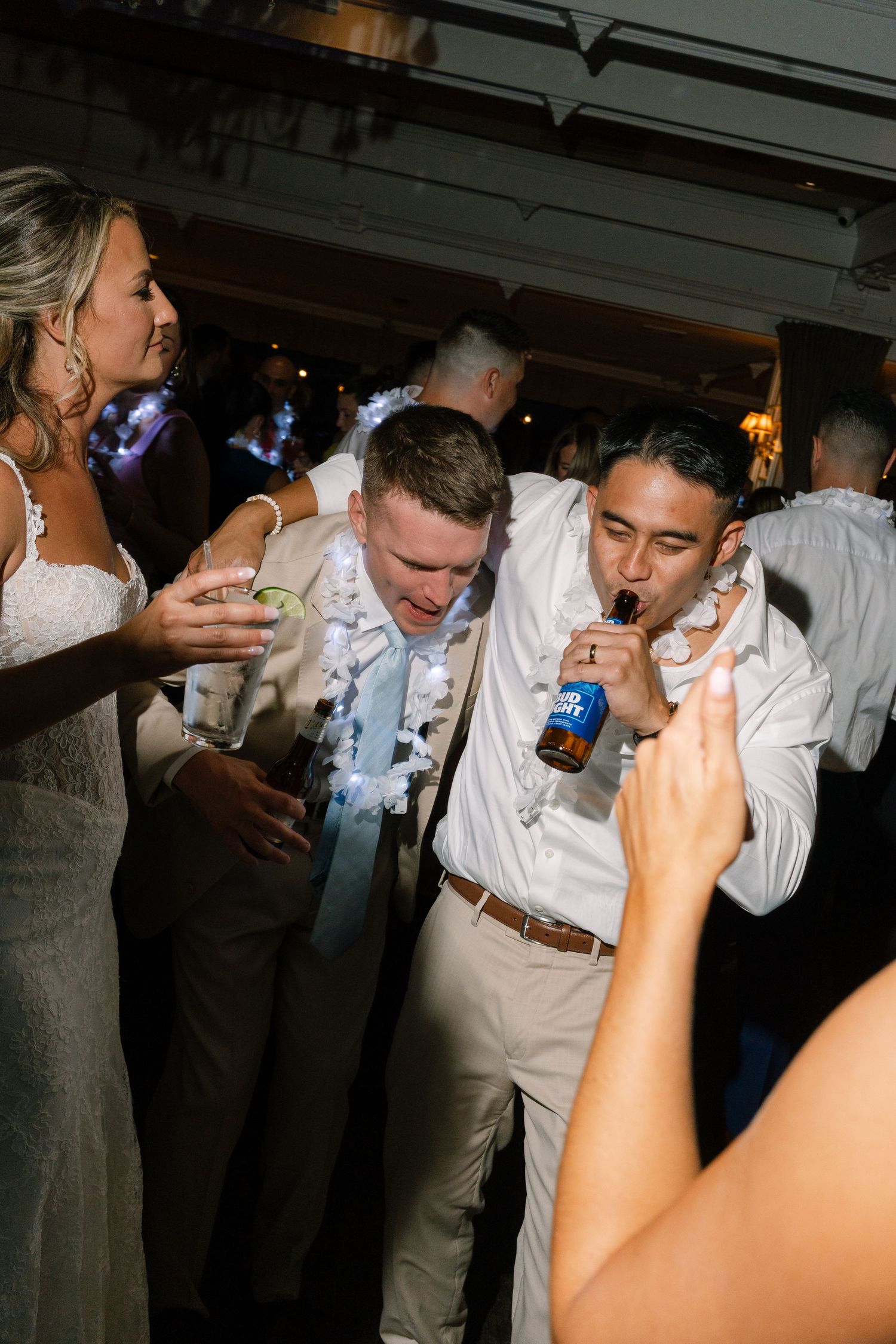 Guests dancing and celebrating at a lively wedding reception, with a man drinking a Bud Light beer.