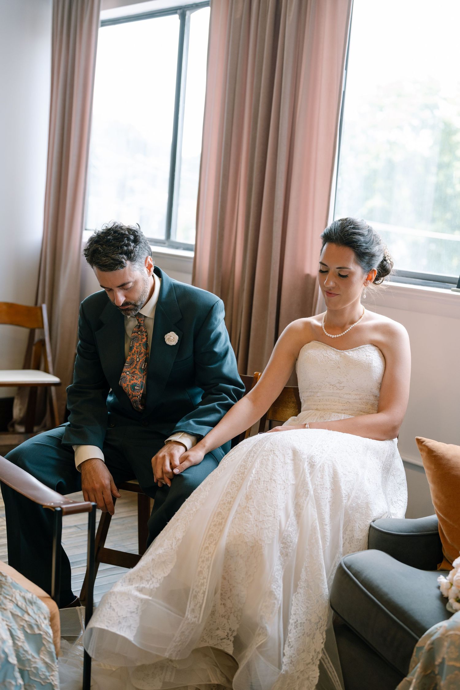 A couple sits together in formal wedding attire looking at a book during a quiet moment.