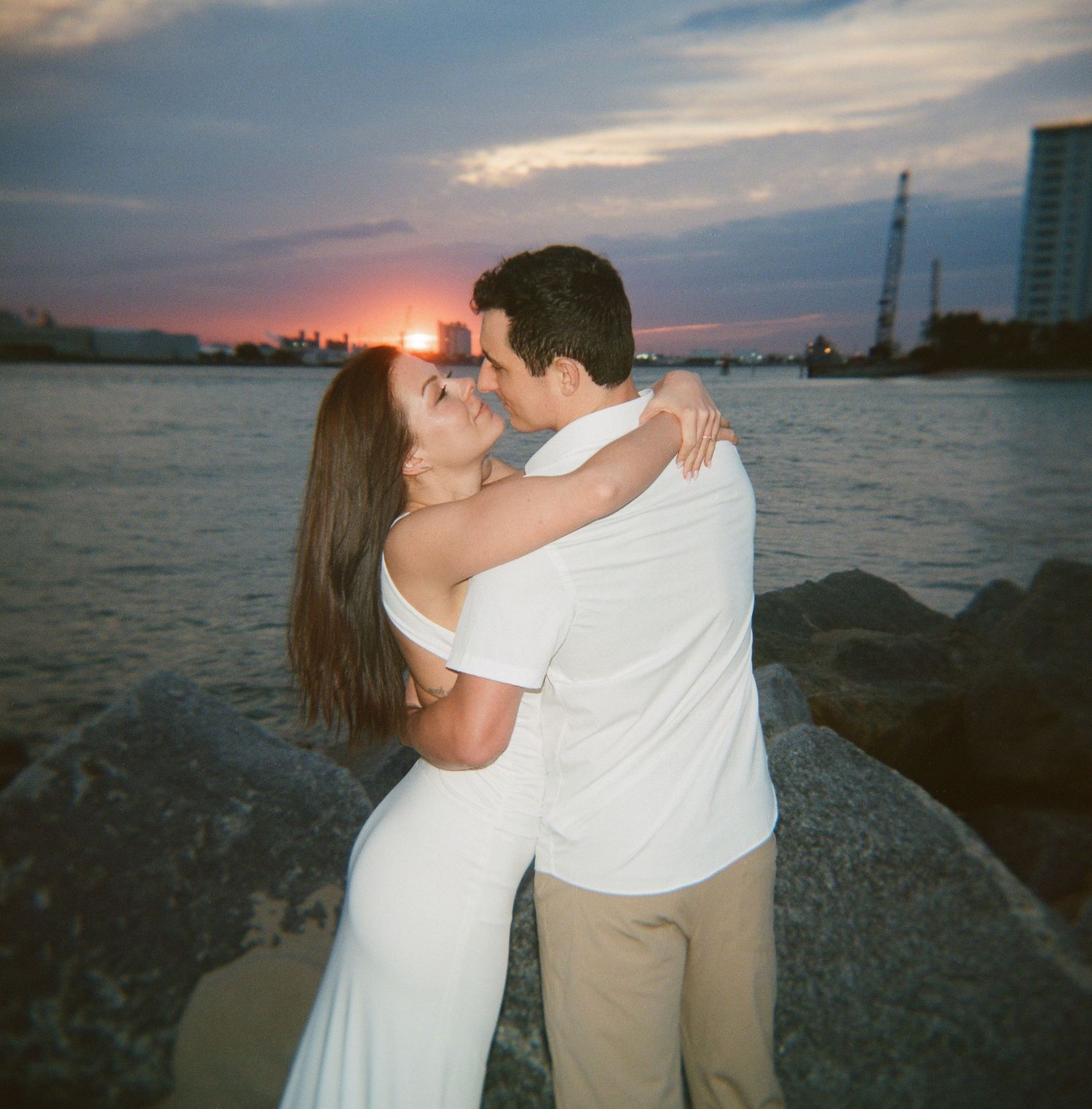Couple embracing on rocky shoreline during a vibrant sunset over the ocean.