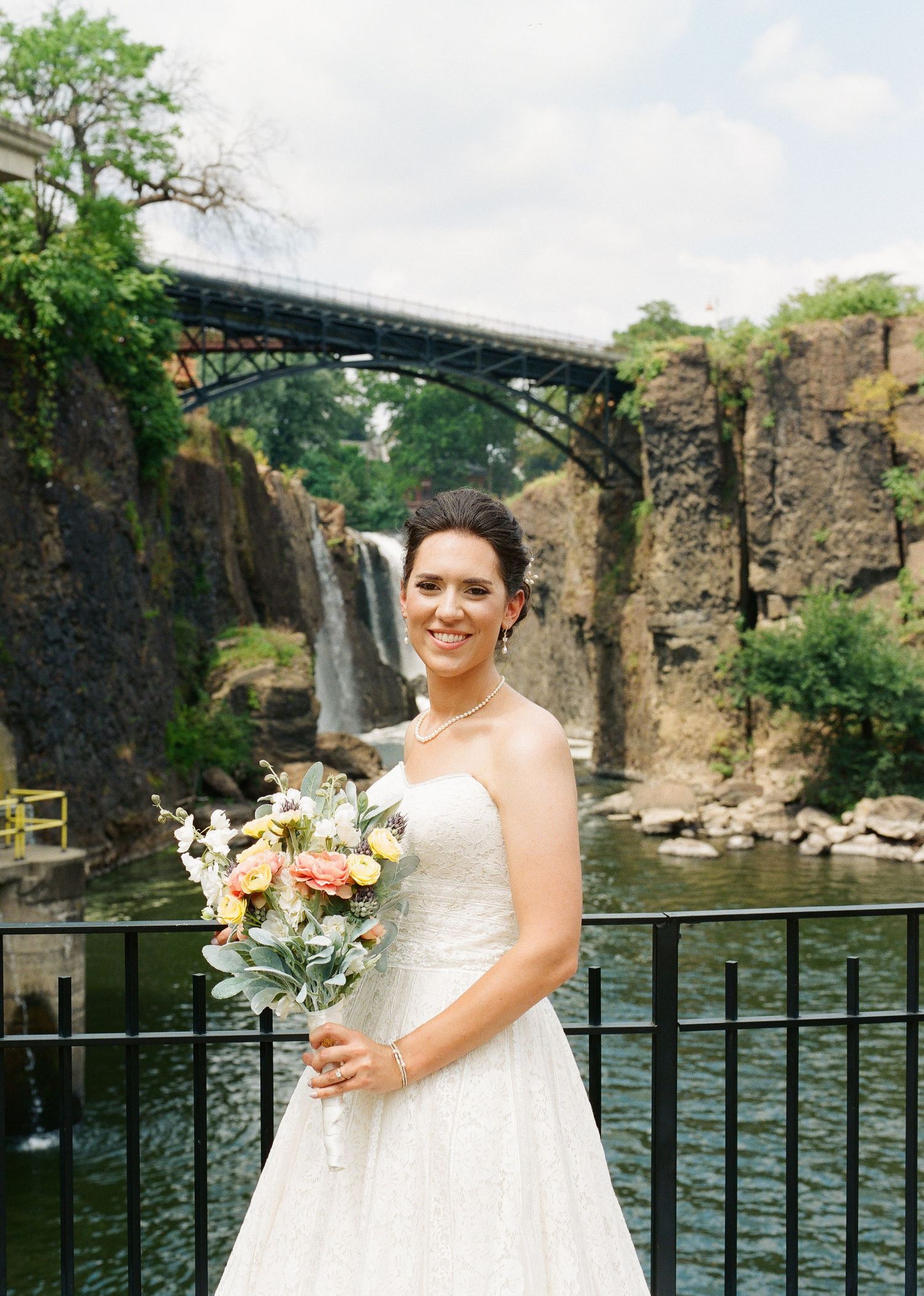 A scenic wedding photo at Paterson Great Falls featuring a white dress and bouquet with a dramatic waterfall backdrop.