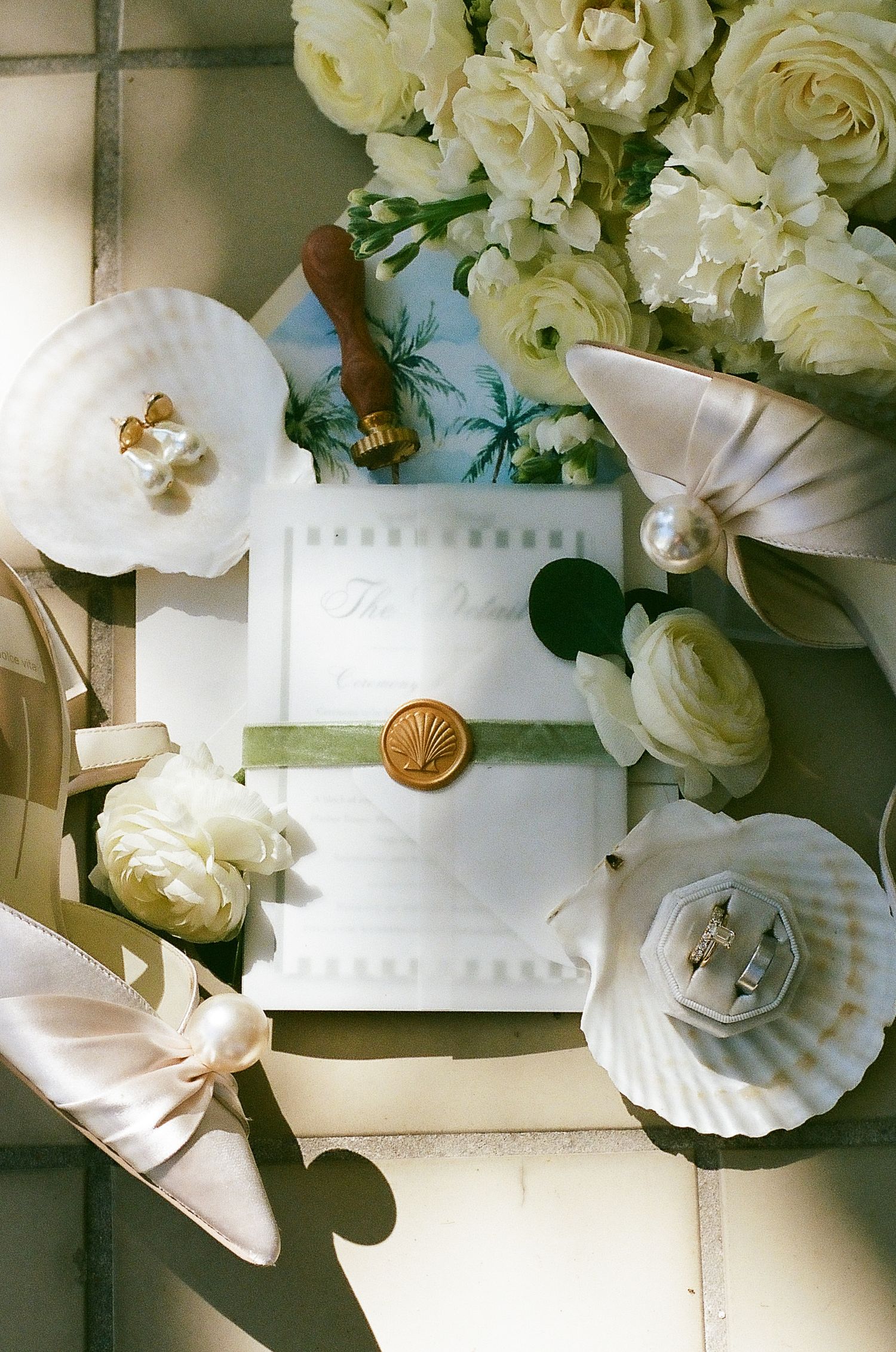 White wedding cake decorated with fresh roses and seashell details sits elegantly on display.