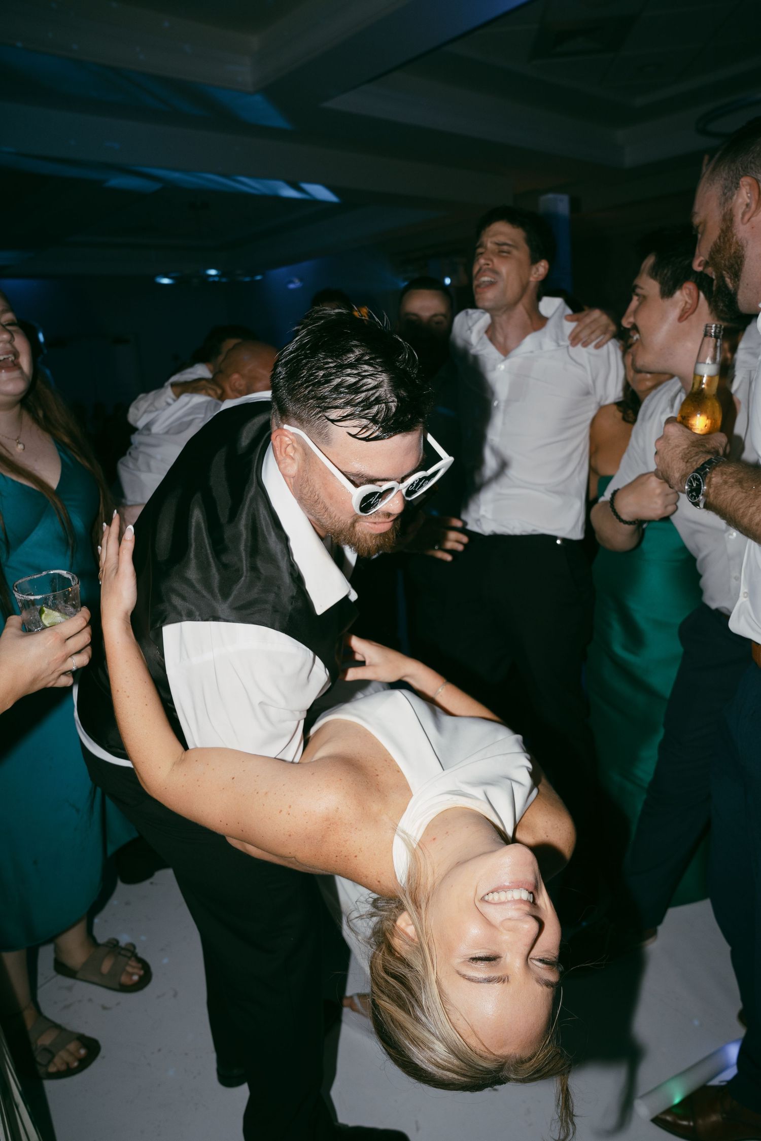 A couple performs a dramatic dance dip move during a wedding reception celebration.