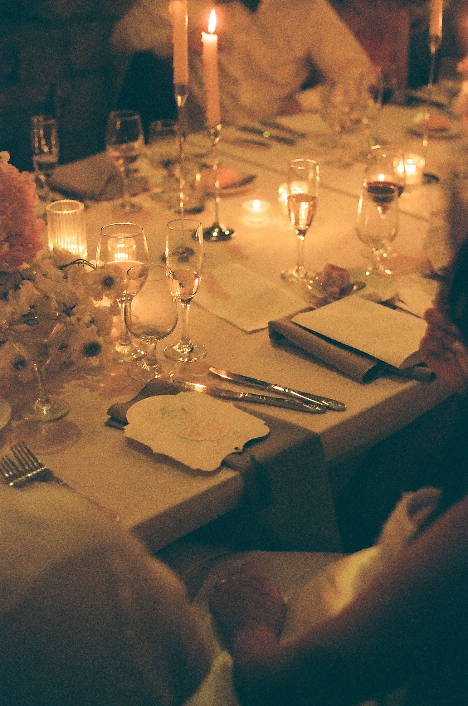 Elegant candlelit wedding reception dinner table with floral centerpieces, glassware, and place settings in warm romantic lighting.