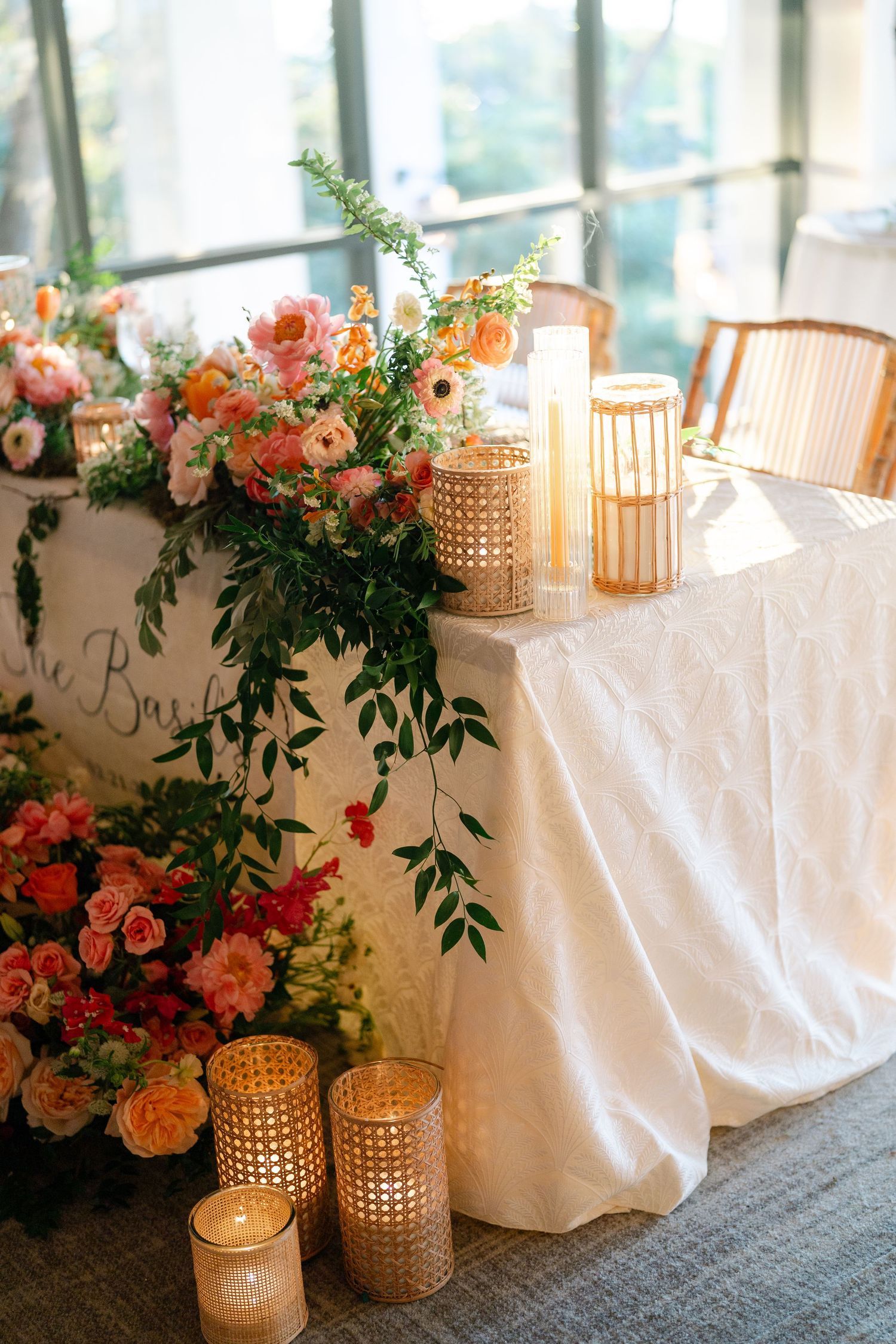 Elegant wedding reception decor with coral floral arrangements and gold lanterns alongside white tablecloths.