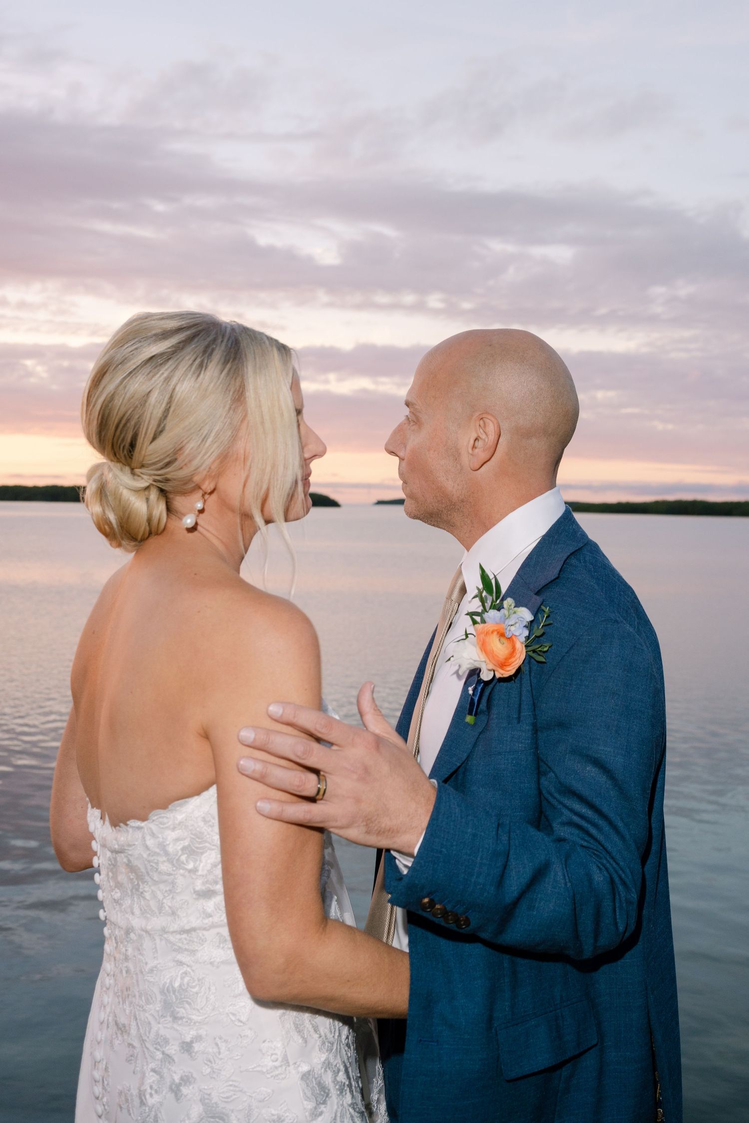 Romantic sunset wedding portrait with ocean backdrop and soft pink sky.