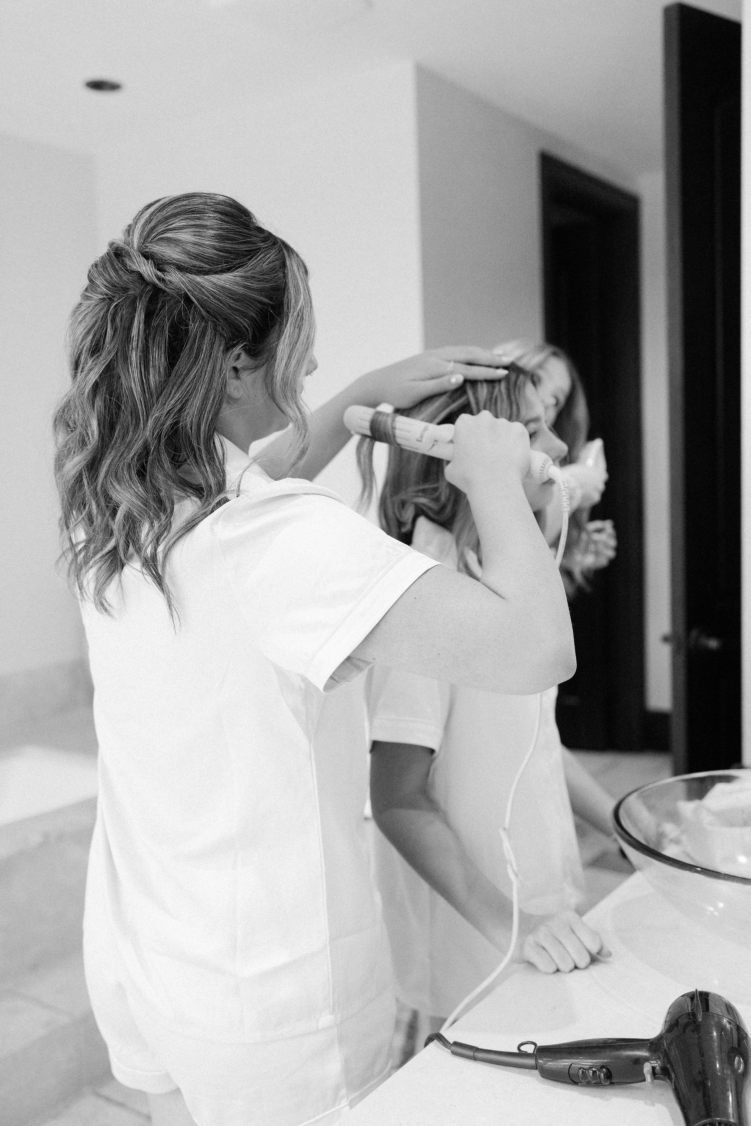 A hairstylist works on styling hair in a bright white room.